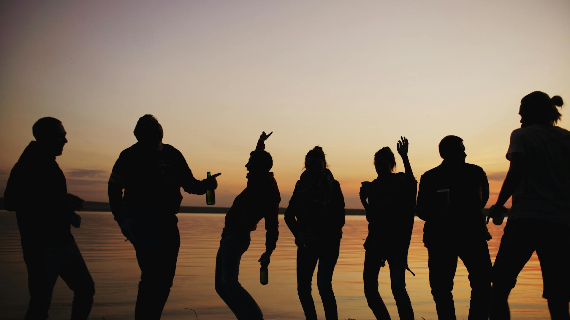 Group of friends silhouetted at sunset by a lake representing the 11th house theme of community and shared joy