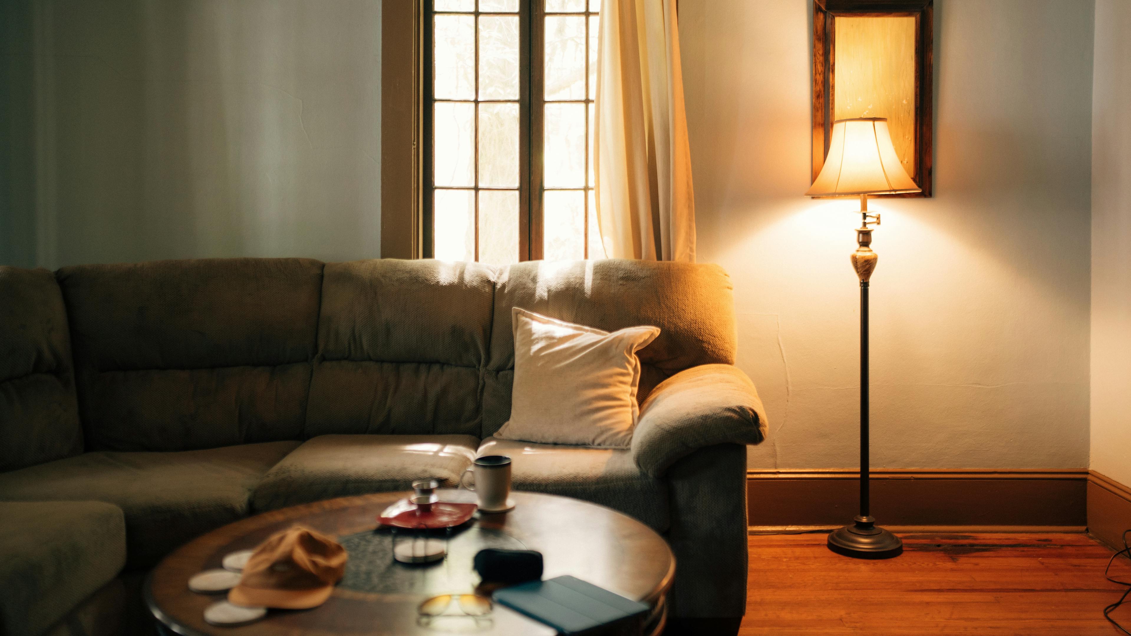 Warm sunlit living room with a sofa and floor lamp representing the sense of home and foundation in the 4th house
