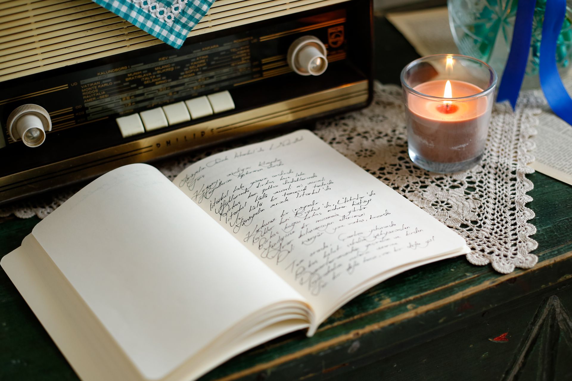 An open journal filled with handwritten cursive beside a lit candle and a vintage radio, set up for a daily 55x5 manifestation writing session
