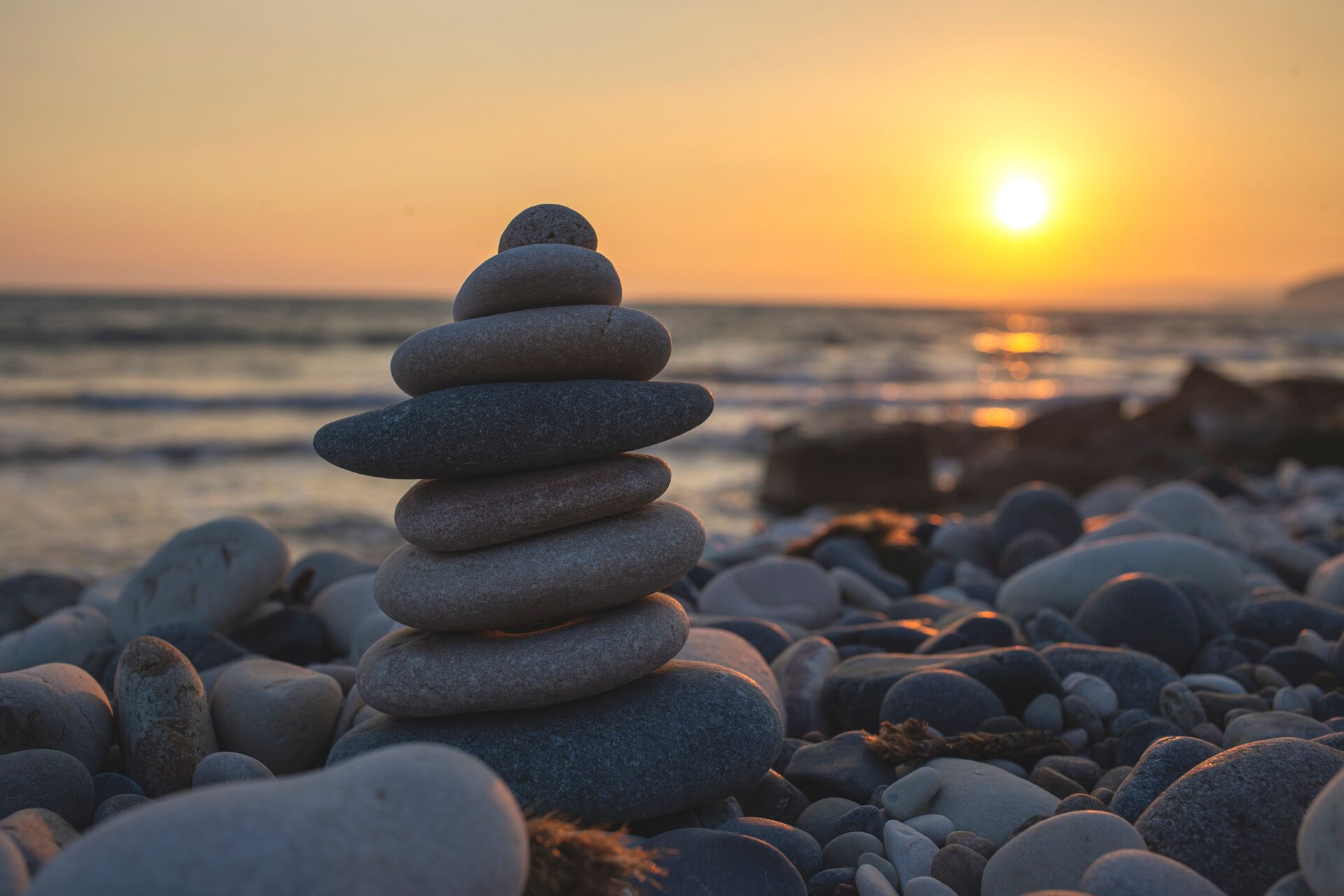 A pair of balanced stones stacked against a calm horizon at sunrise, representing the harmony of the numbers one and two in angel number 1212