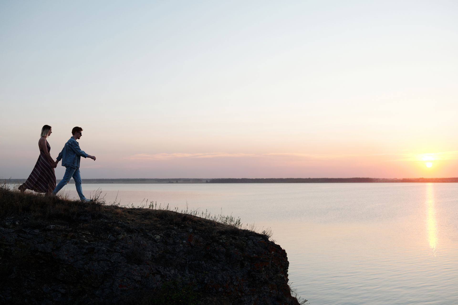 A couple holding hands and walking along a cliff above calm water at sunset, symbolizing the deep, authentic love connected to angel number 777