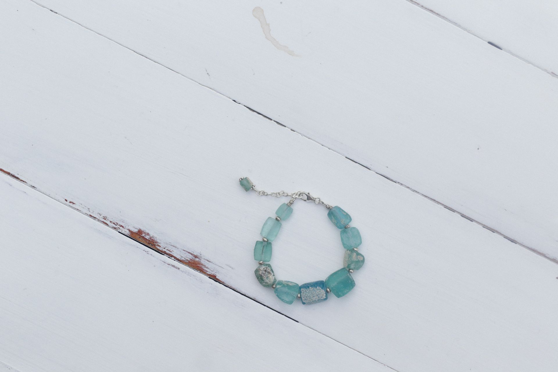 A pale blue-green aquamarine beaded bracelet resting on white painted wood