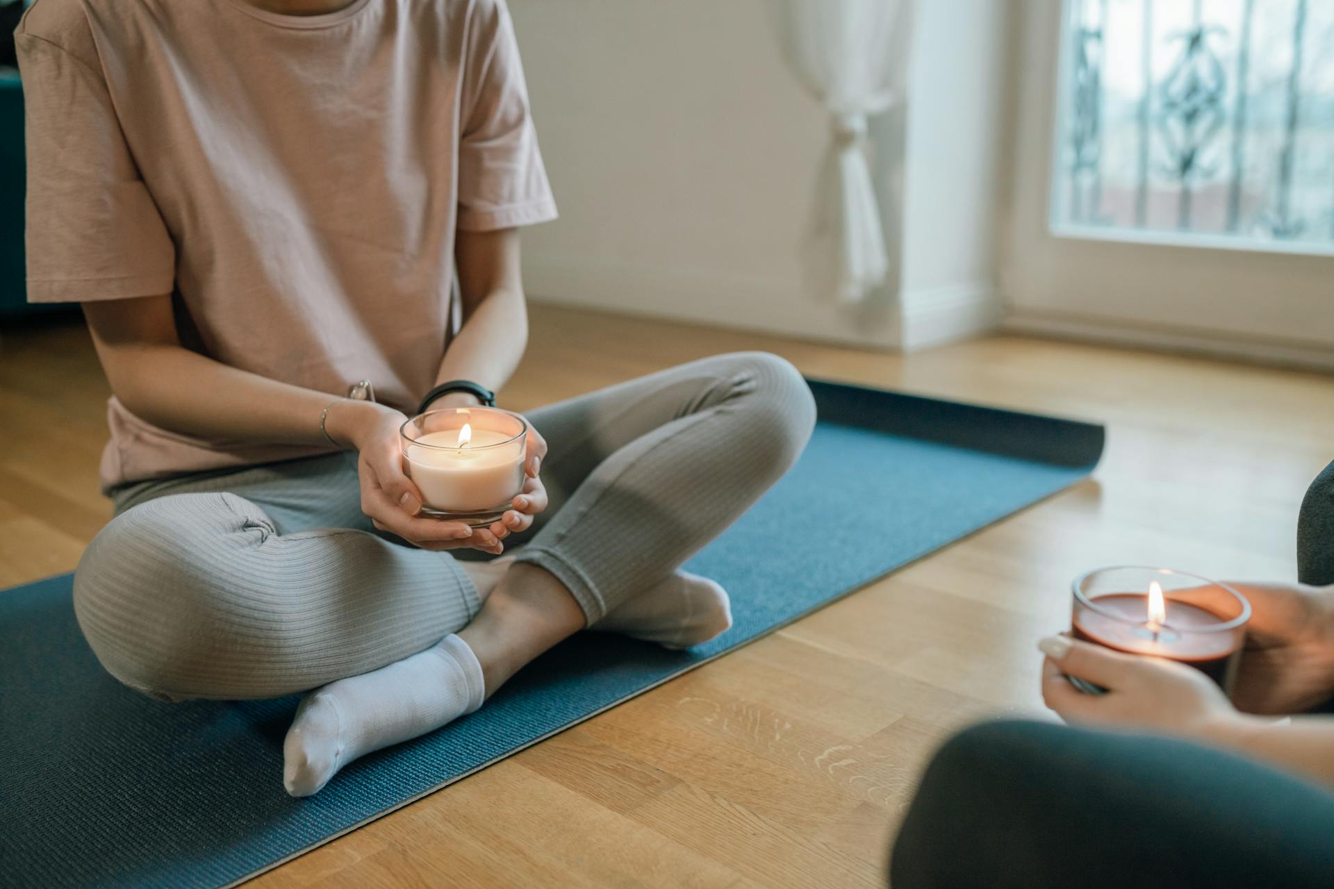 A woman in activewear meditating with a lit candle representing mindful wellness practices connected to astrological self-care