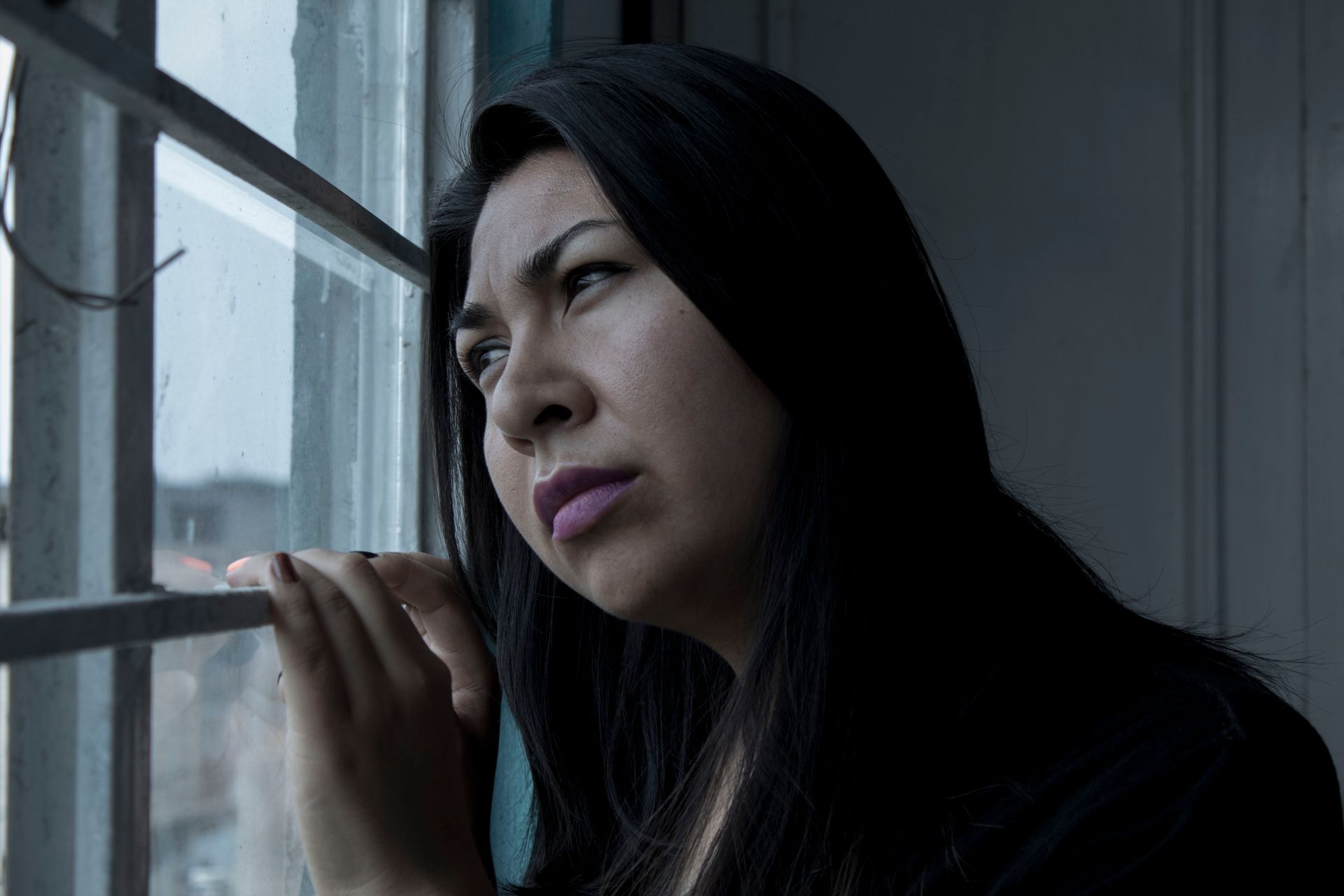 A person sitting alone by a window in soft light, reflecting the inward pull of anxious and avoidant attachment