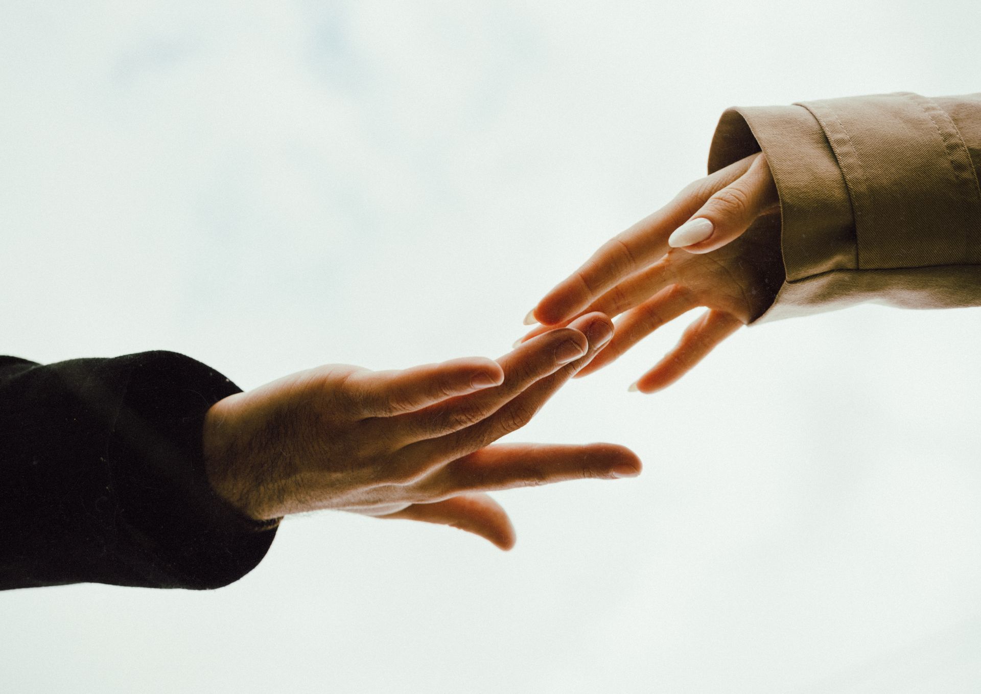 Two hands reaching toward each other in soft light, representing the pull toward closeness in attachment