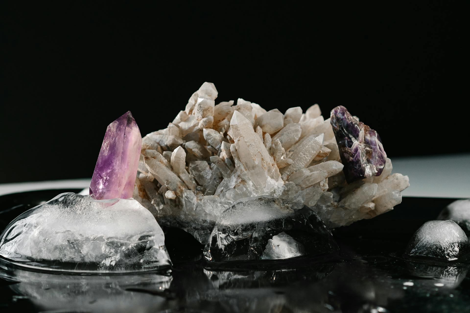 Amethyst and clear quartz crystals resting on ice against a dark reflective surface capturing the mysterious beauty of zodiac gemstones