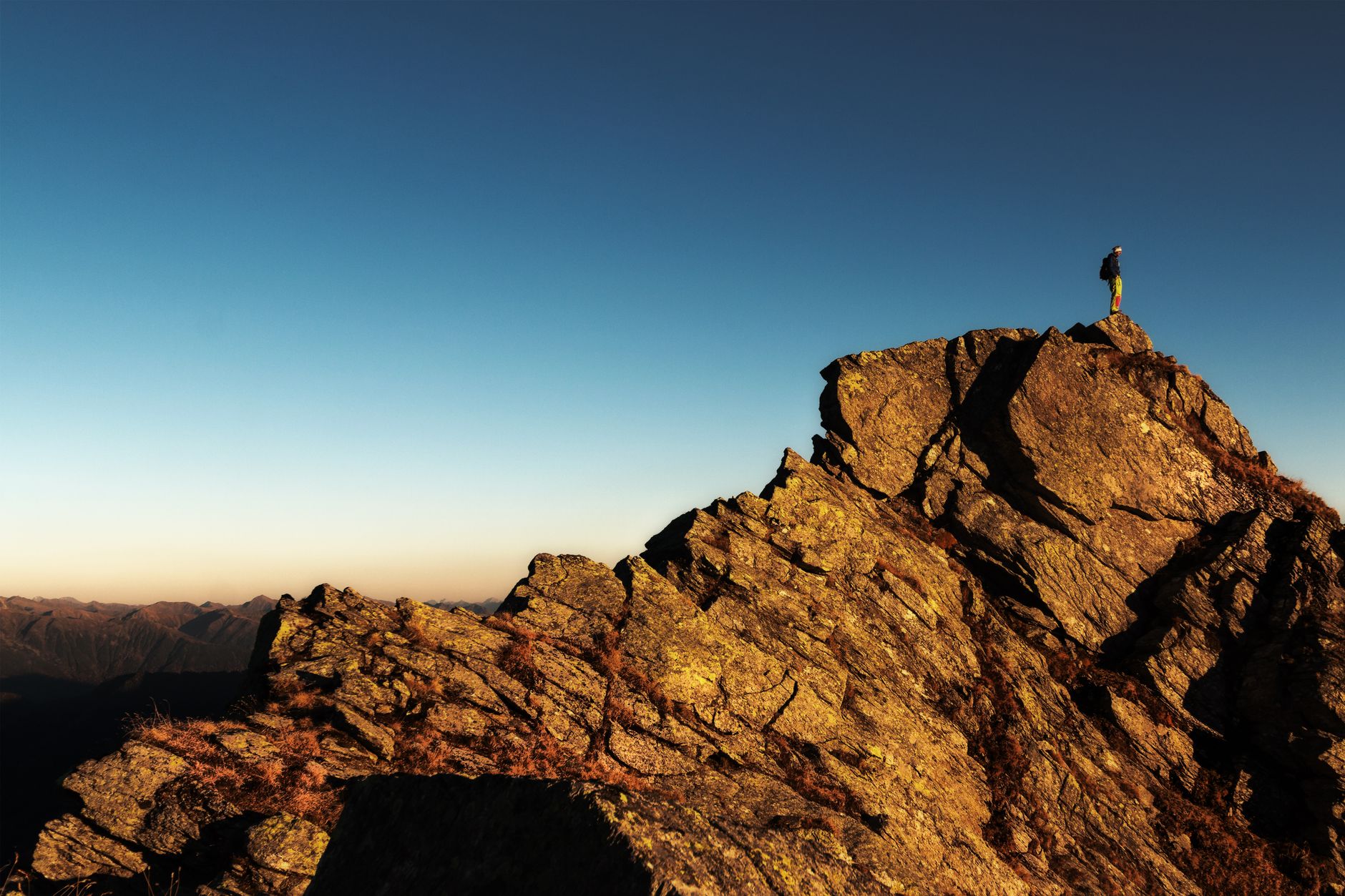 A lone climber nearing a high mountain summit at sunrise, reflecting the Capricorn drive to reach the top through patience and effort