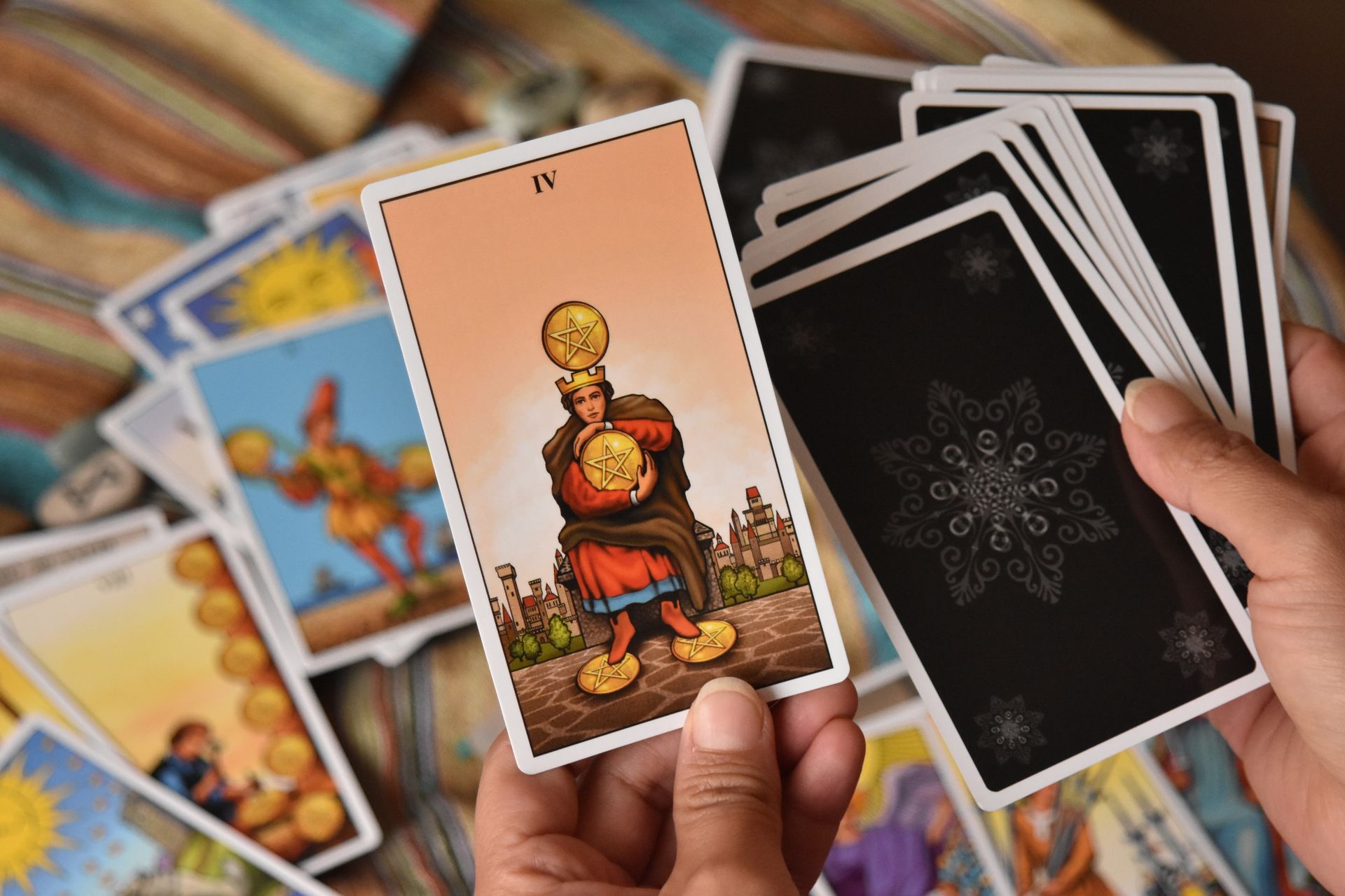 A hand holding a fully illustrated Rider-Waite-Smith style tarot card above a fanned deck, showing why scenic cards are easier for beginners to read