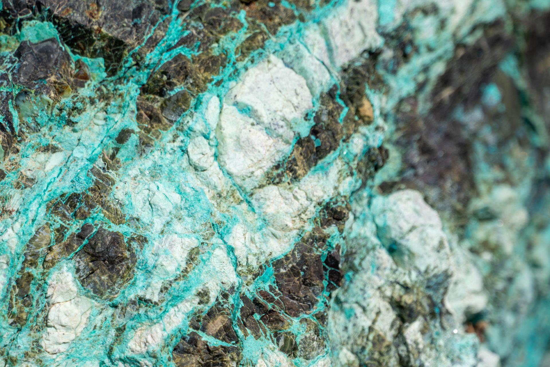 A close-up of natural chrysocolla, a blue-green copper mineral veining through a rocky quartz matrix, illustrating chrysocolla meaning as a stone of calm communication