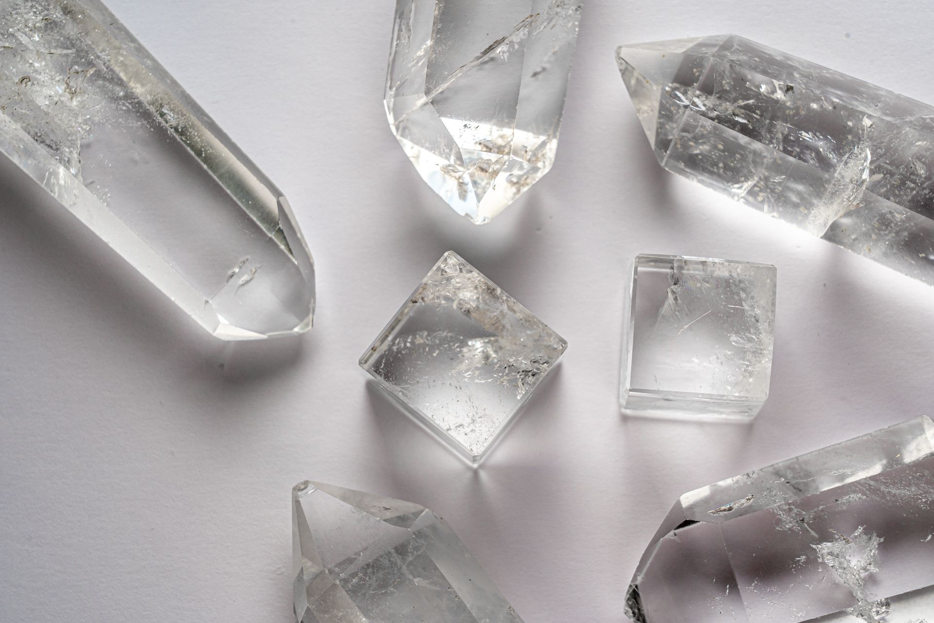 Clear quartz and mixed quartz crystals arranged neatly on a white surface, the kind of amplifying stones often used at the center of a crystal grid