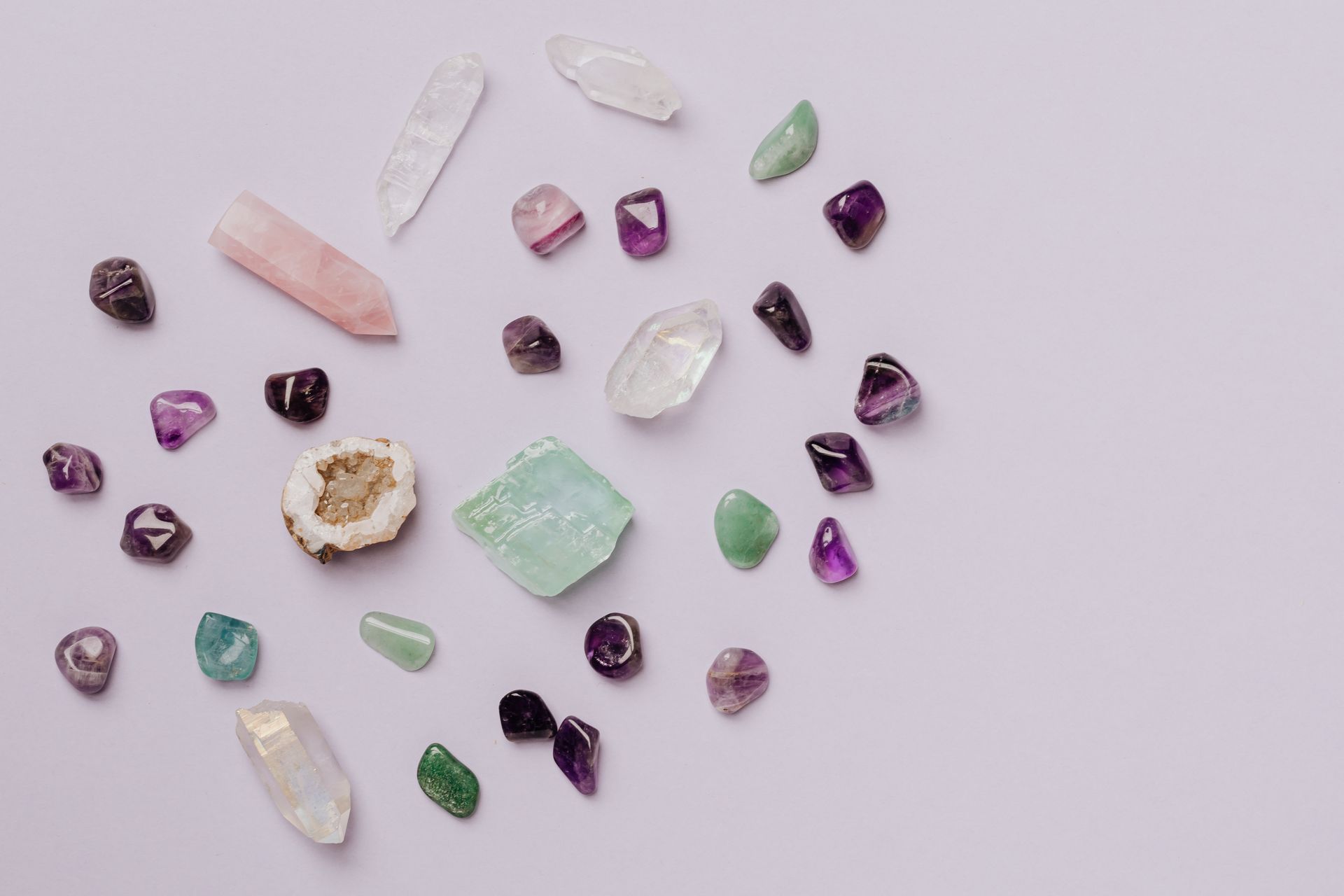 A selection of tumbled healing crystals and gemstones laid out on a light surface, ready to be chosen for a crystal grid