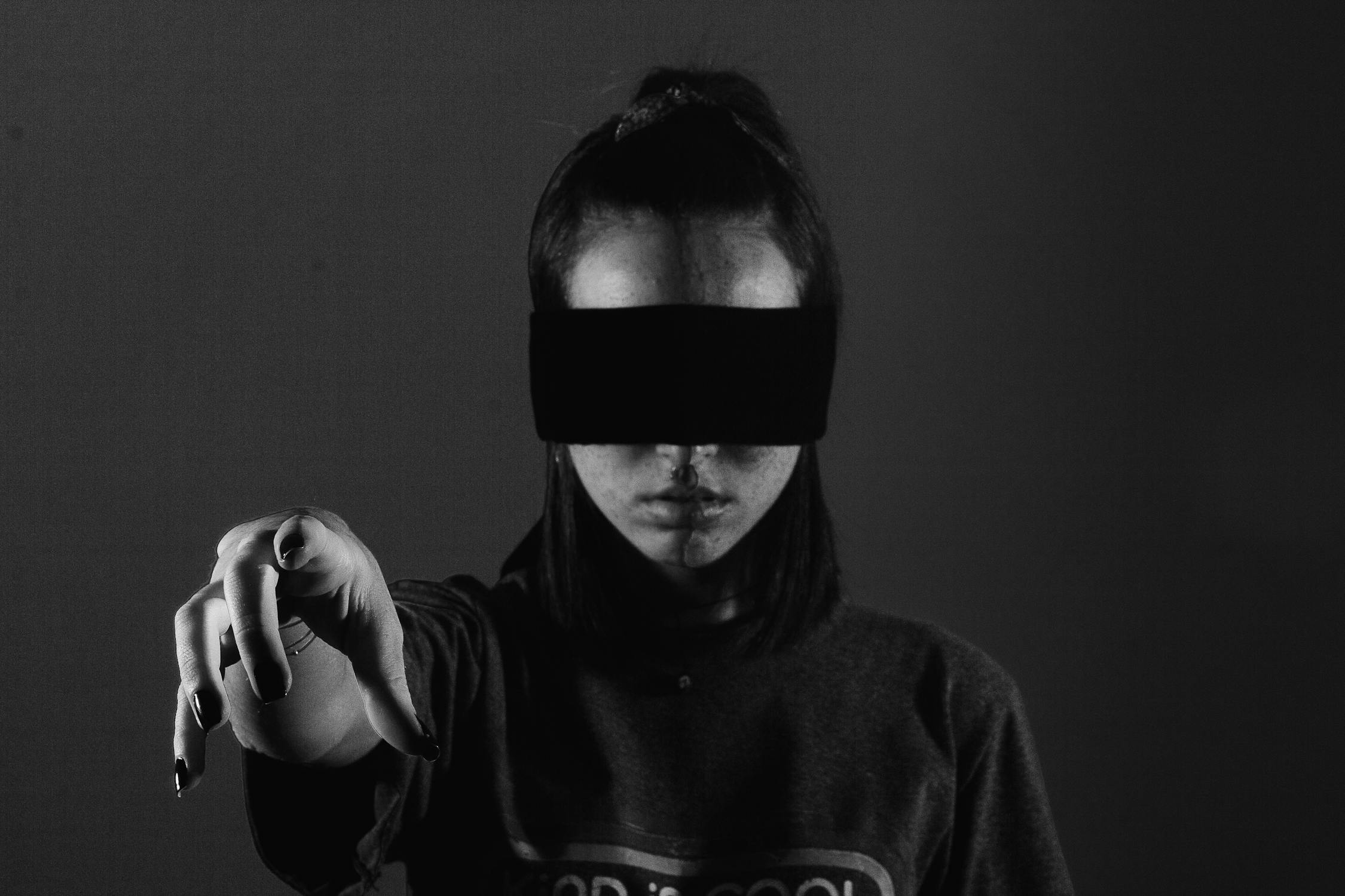 A blindfolded woman reaching forward in dramatic black and white creating a mysterious mood that captures the Eight of Swords energy of searching for an unseen exit