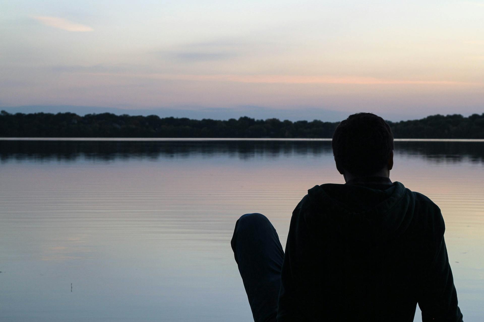 A person relaxing by a tranquil lake during sunset reflecting the peaceful solitude and restorative stillness that the Four of Swords prescribes