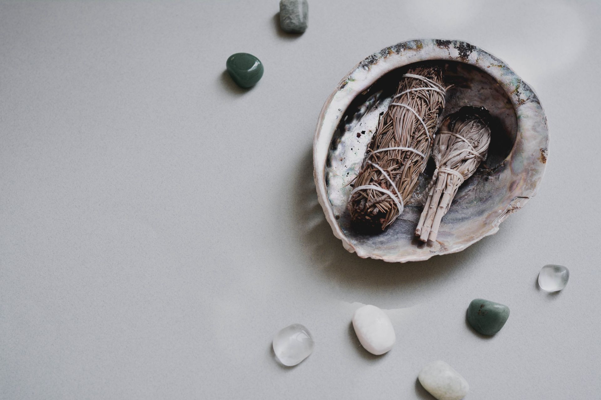 Tumbled crystals being cleansed with the smoke of a burning sage bundle, a safe way to clear water-sensitive stones