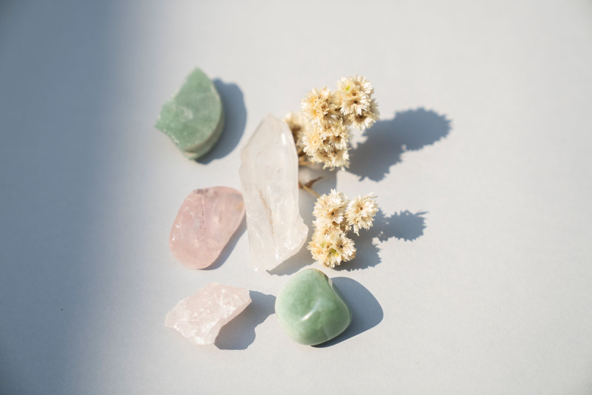 A polished green aventurine tumbled stone beside rose quartz and clear quartz in soft light, representing green aventurine meaning and healing properties