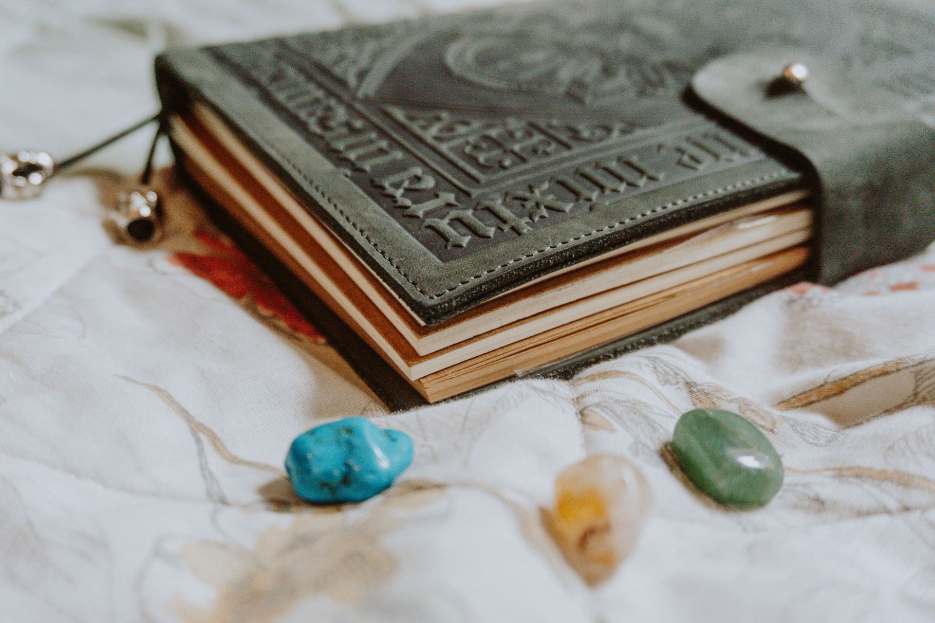 Green aventurine and other polished tumbled stones resting beside a leather journal, showing the stone's soft shimmer