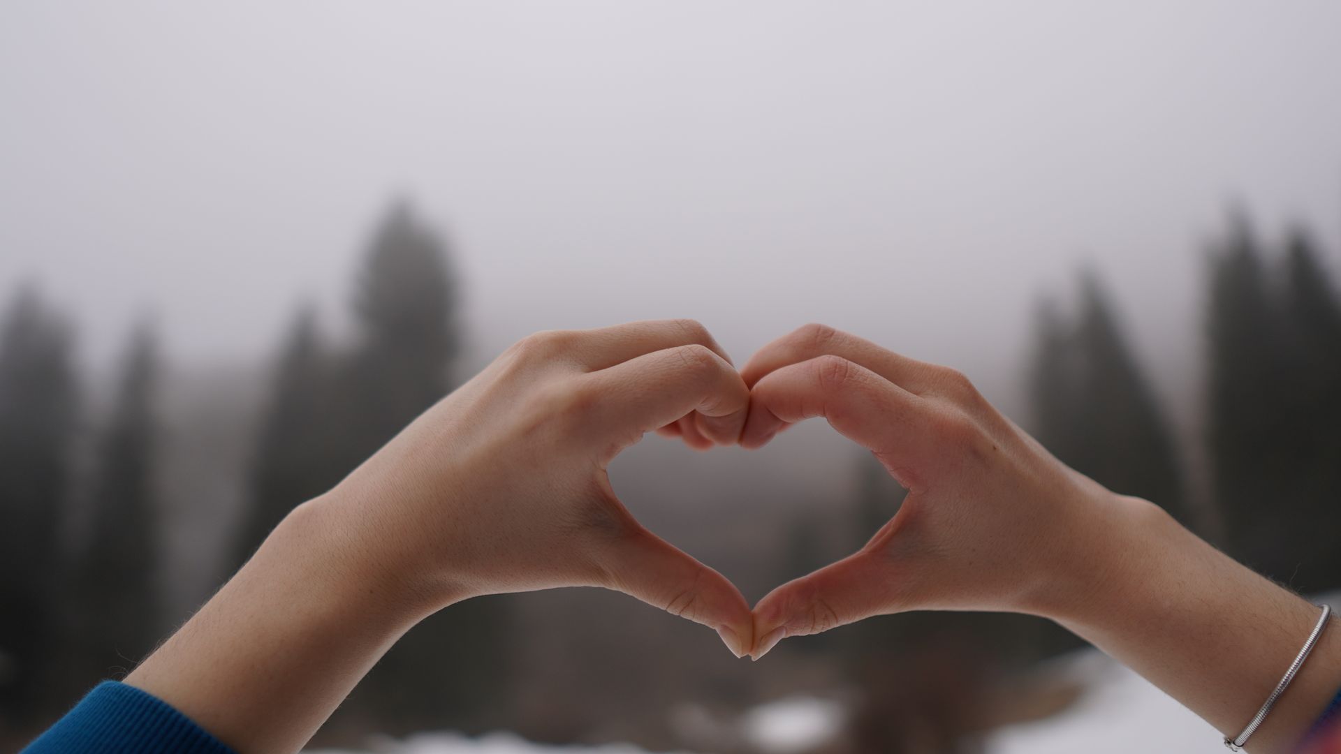 Two hands forming a heart shape against a soft green misty forest, evoking the green color and loving, open energy of a balanced heart chakra