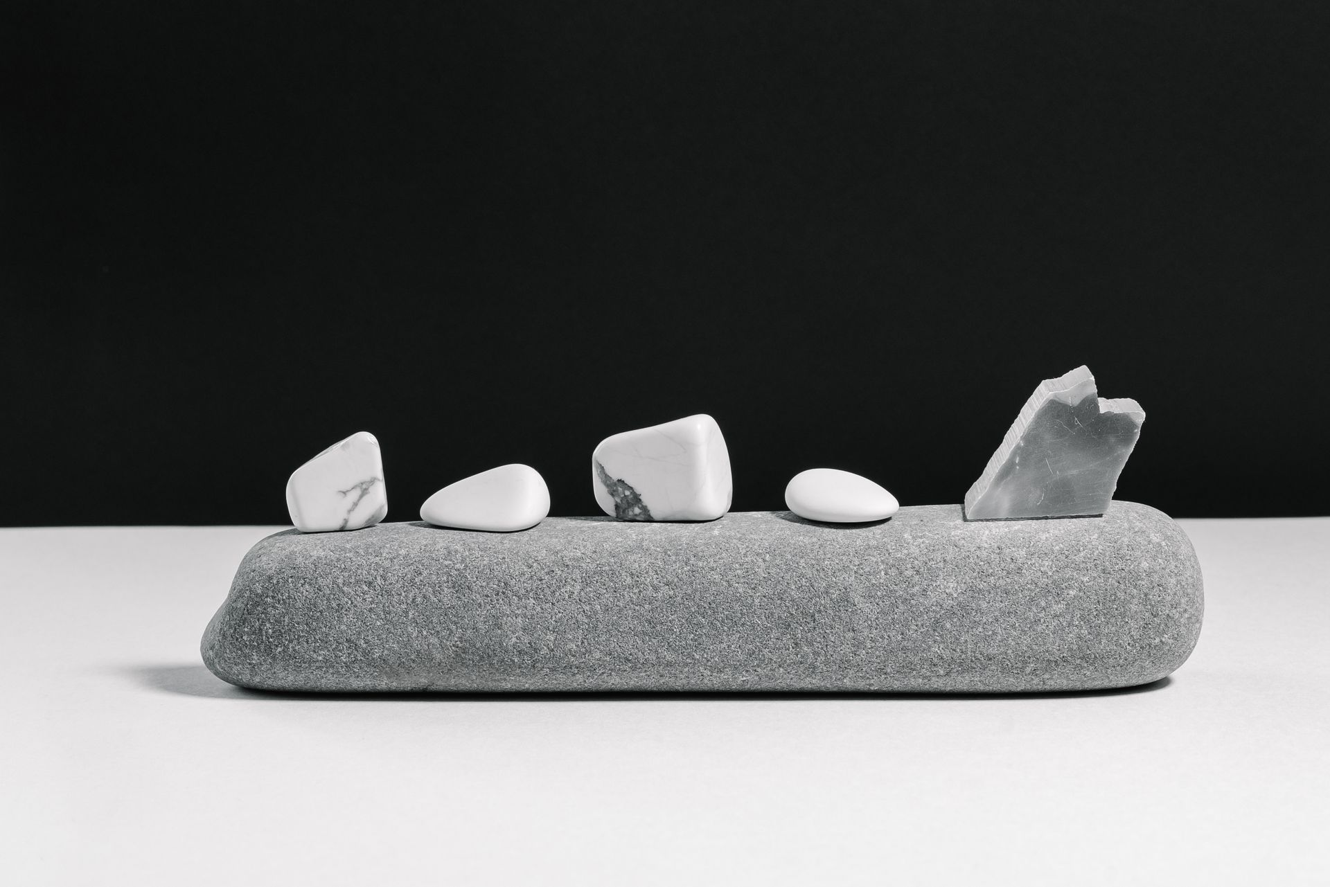 White tumbled howlite stones with natural gray web-like veining resting on a smooth gray river stone, illustrating howlite meaning as a calming stone