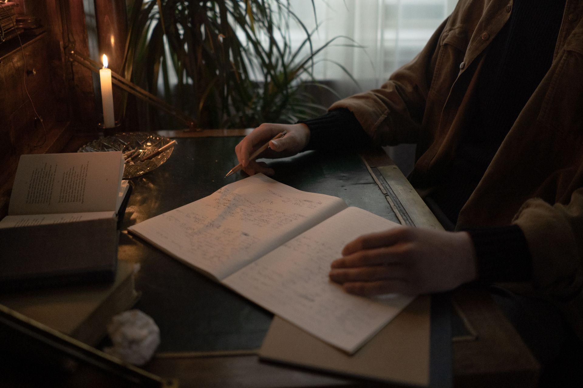 Person writing in a journal by candlelight surrounded by open books, studying their human design chart
