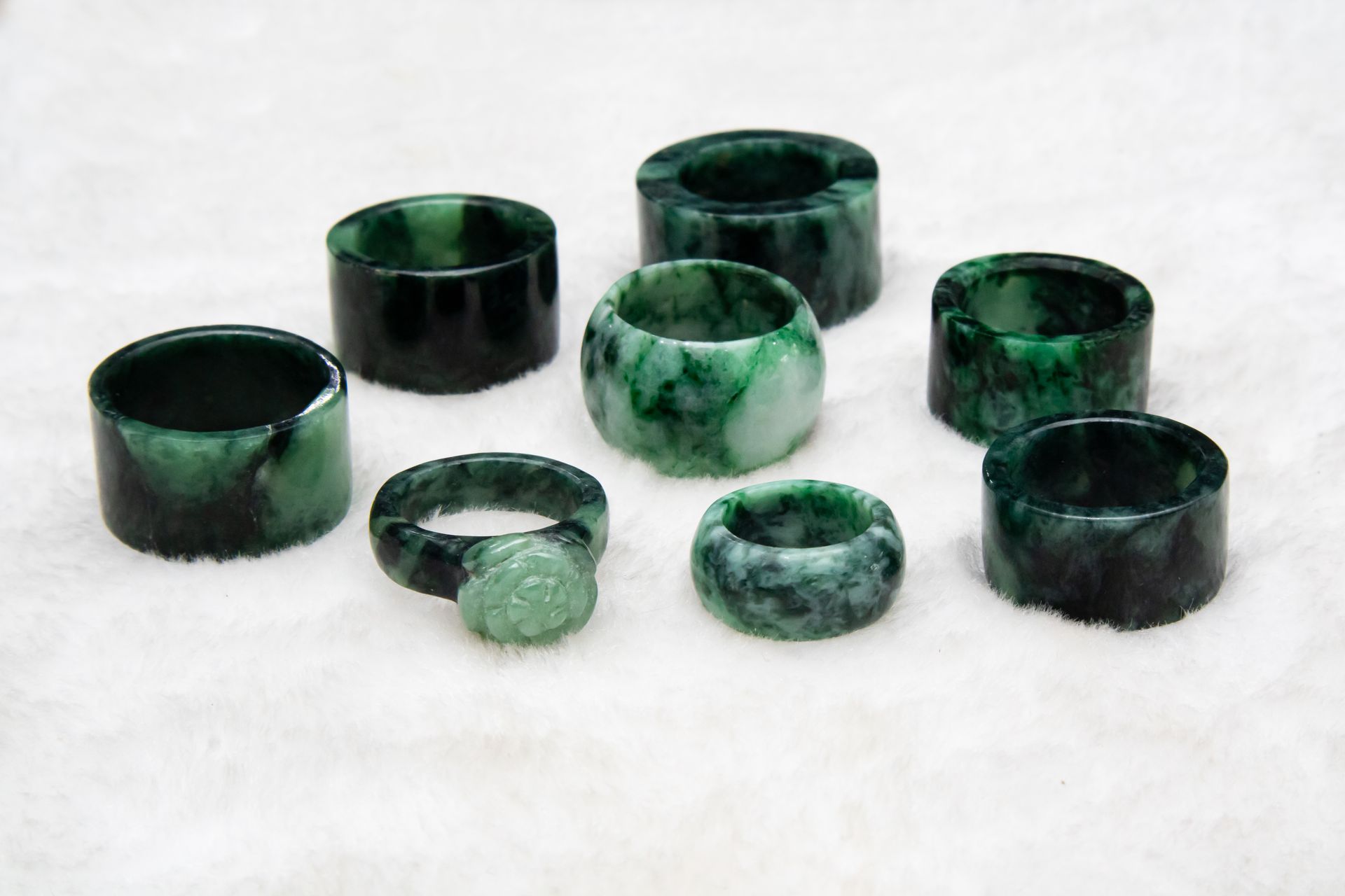 A collection of polished green jade rings with mottled green markings resting on soft white fabric, representing jade meaning and healing properties