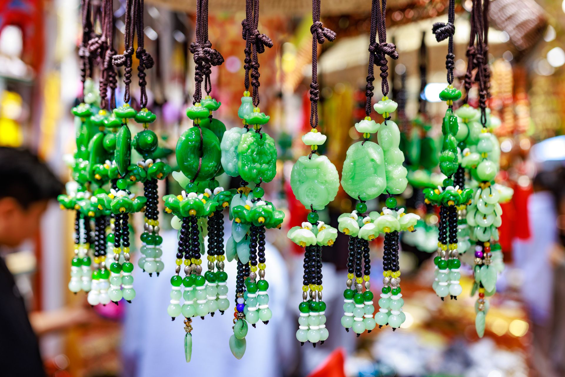 Carved green jade pendants and ornaments hanging on cords at a traditional market stall