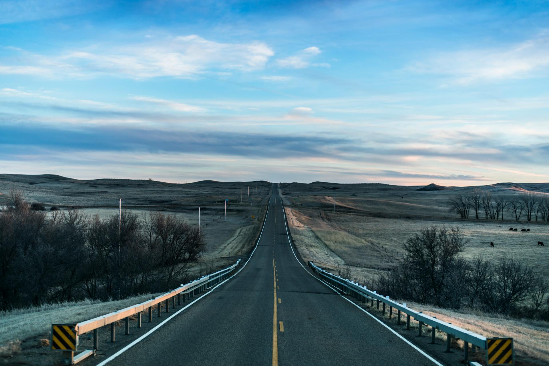 A straight road through open prairie stretching toward a wide horizon under an expansive sky