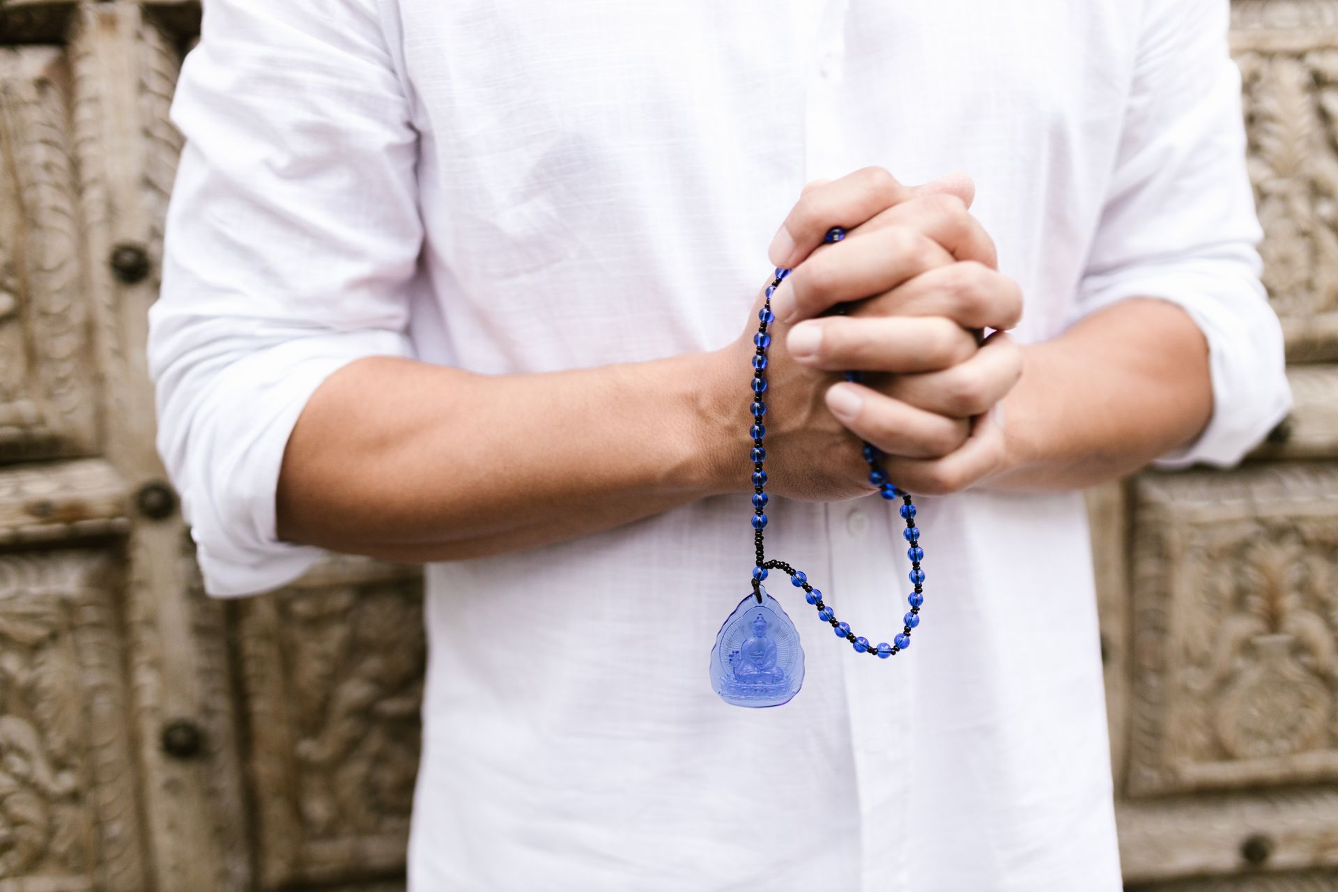 A person holding blue prayer beads in meditation, representing lapis lazuli and the throat and third eye chakras