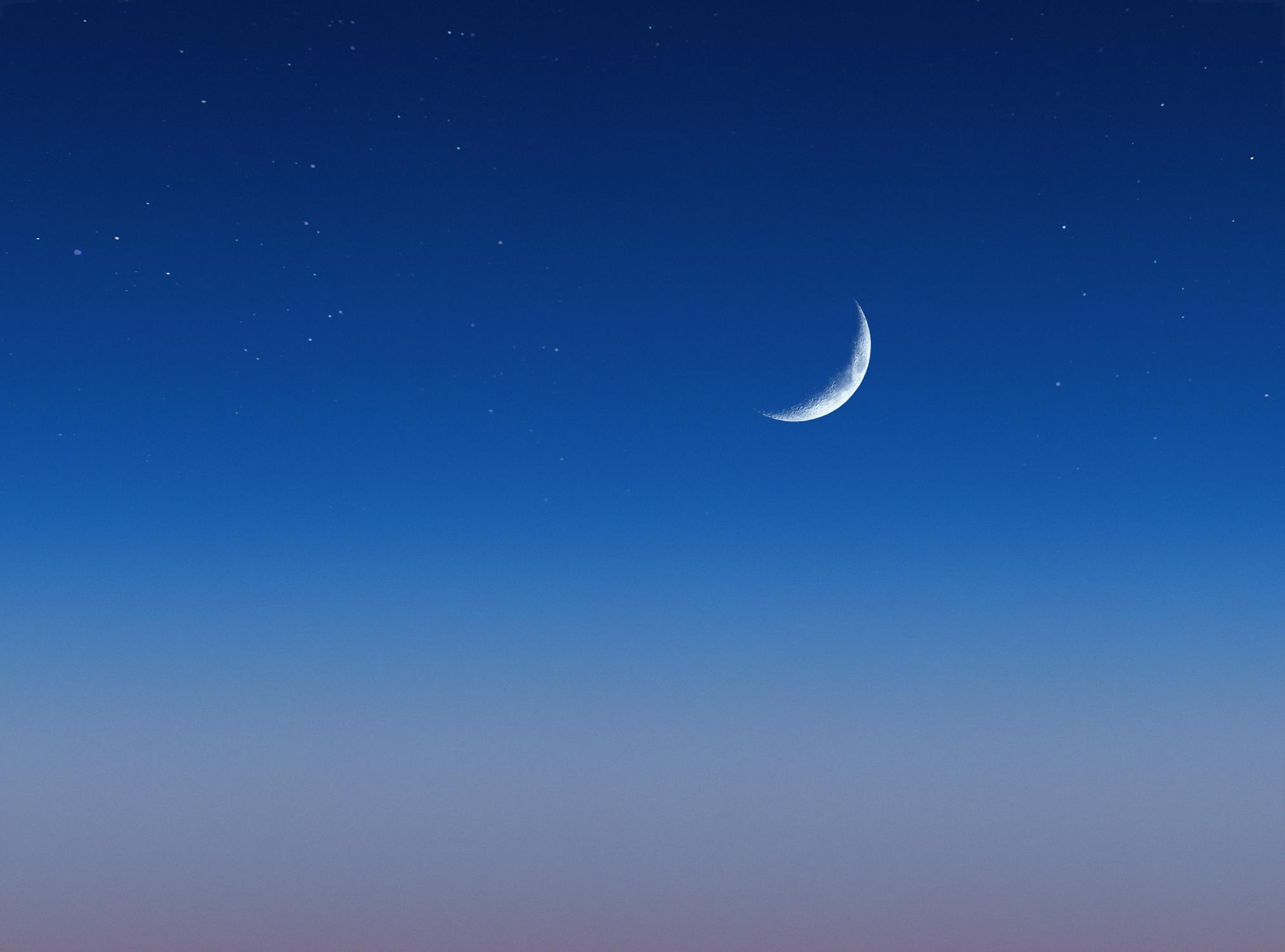 A serene crescent moon against a deep blue sky scattered with stars representing the monthly lunar cycle