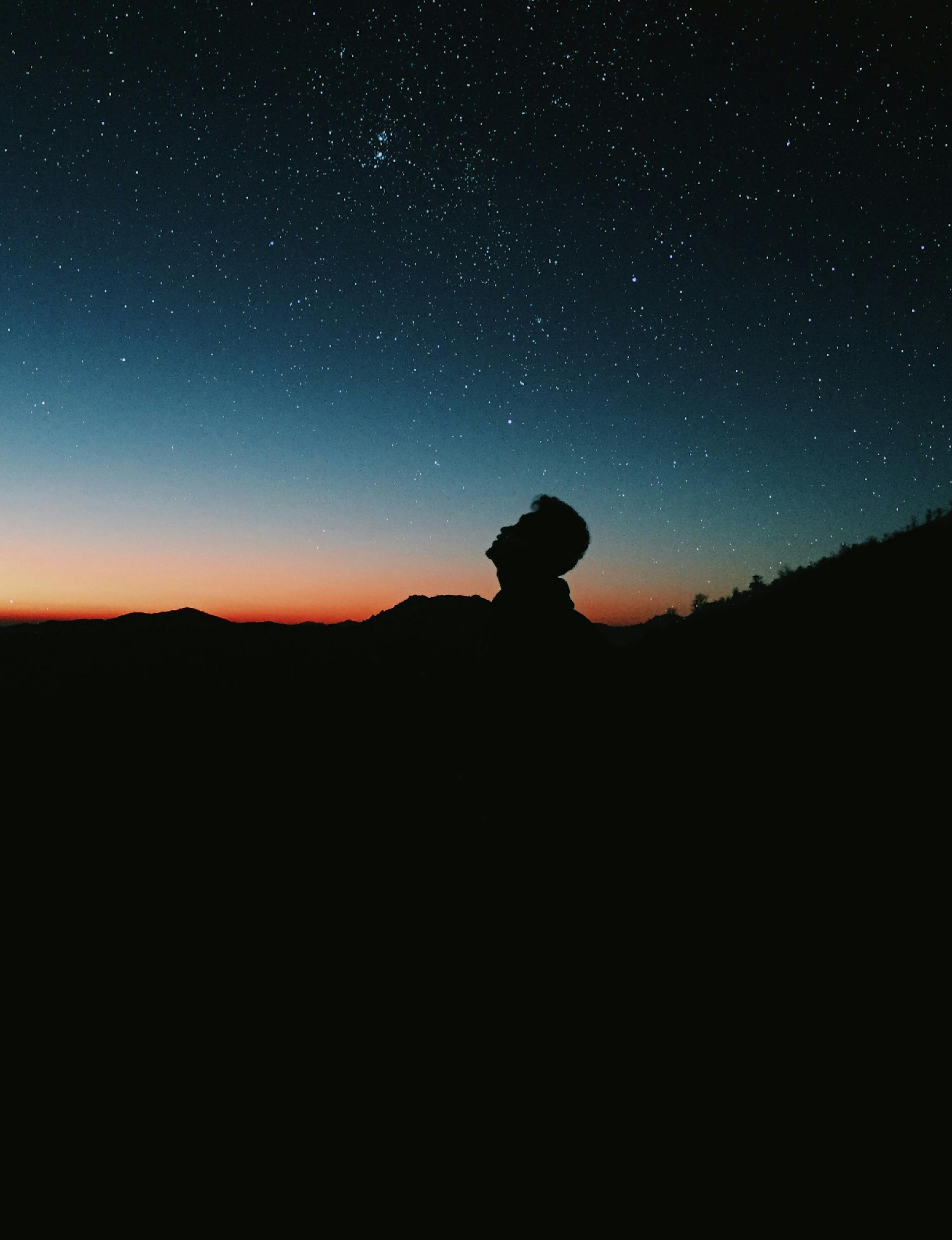 A person silhouetted against a vibrant starry sky representing the ancient connection between celestial bodies and human health