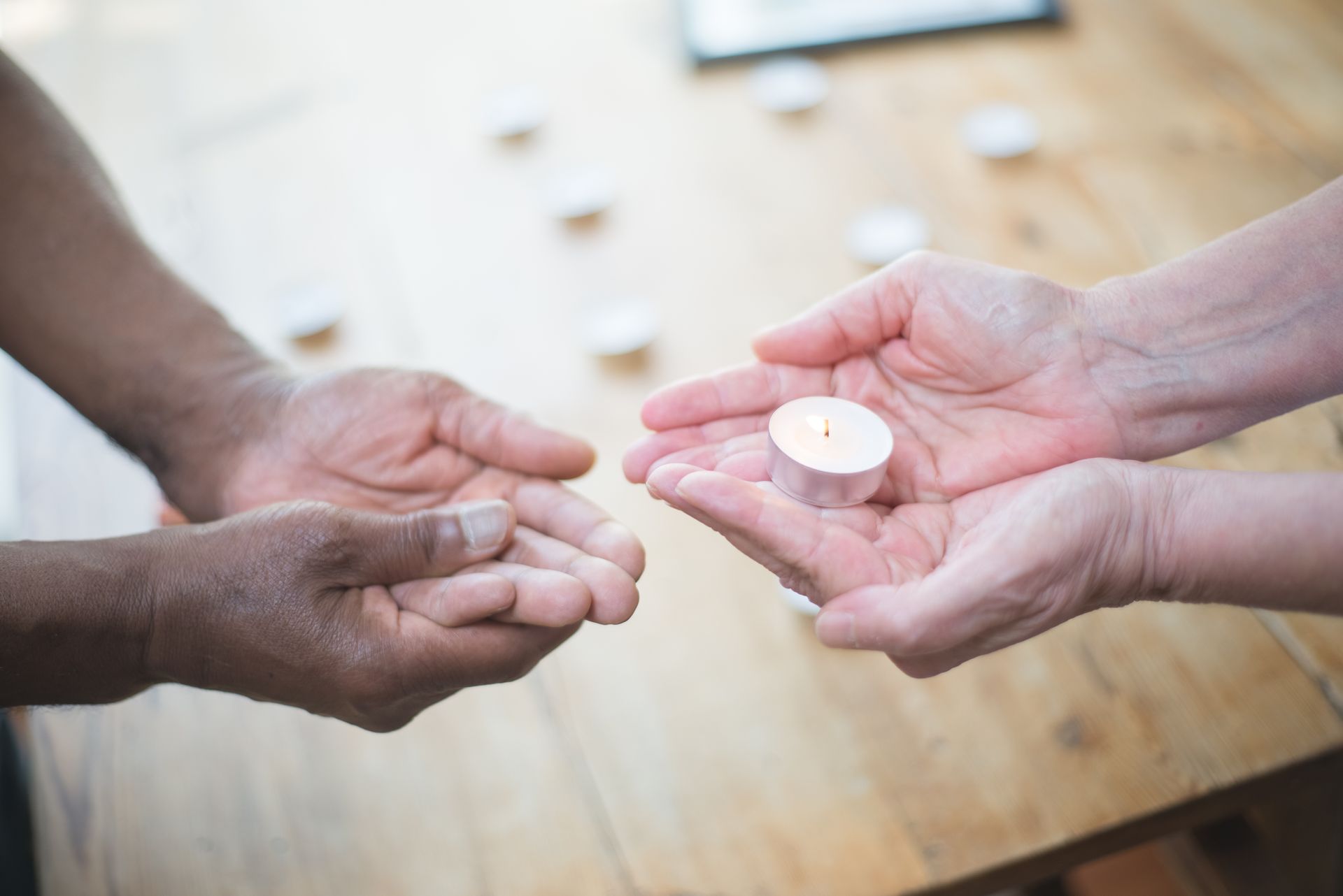 Two hands exchanging a lit candle across a table, symbolizing two planets passing strength to each other