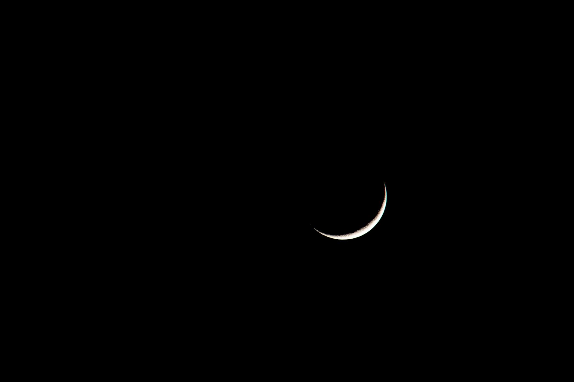 A thin crescent moon glowing against a deep dark sky representing the forward-pushing energy of the crescent natal phase