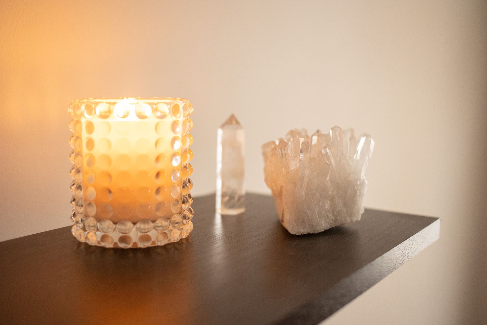 A warmly lit candle and crystals on a wooden shelf, representing how to cleanse and care for oracle cards