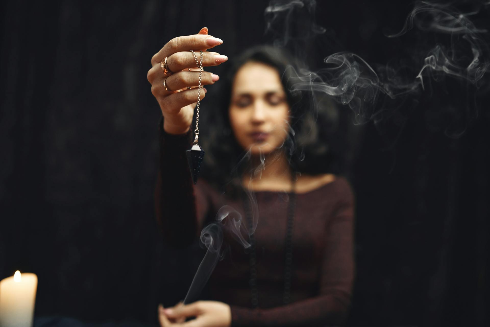 A woman holding a pendulum with smoke creating a mystical atmosphere around the divination practice