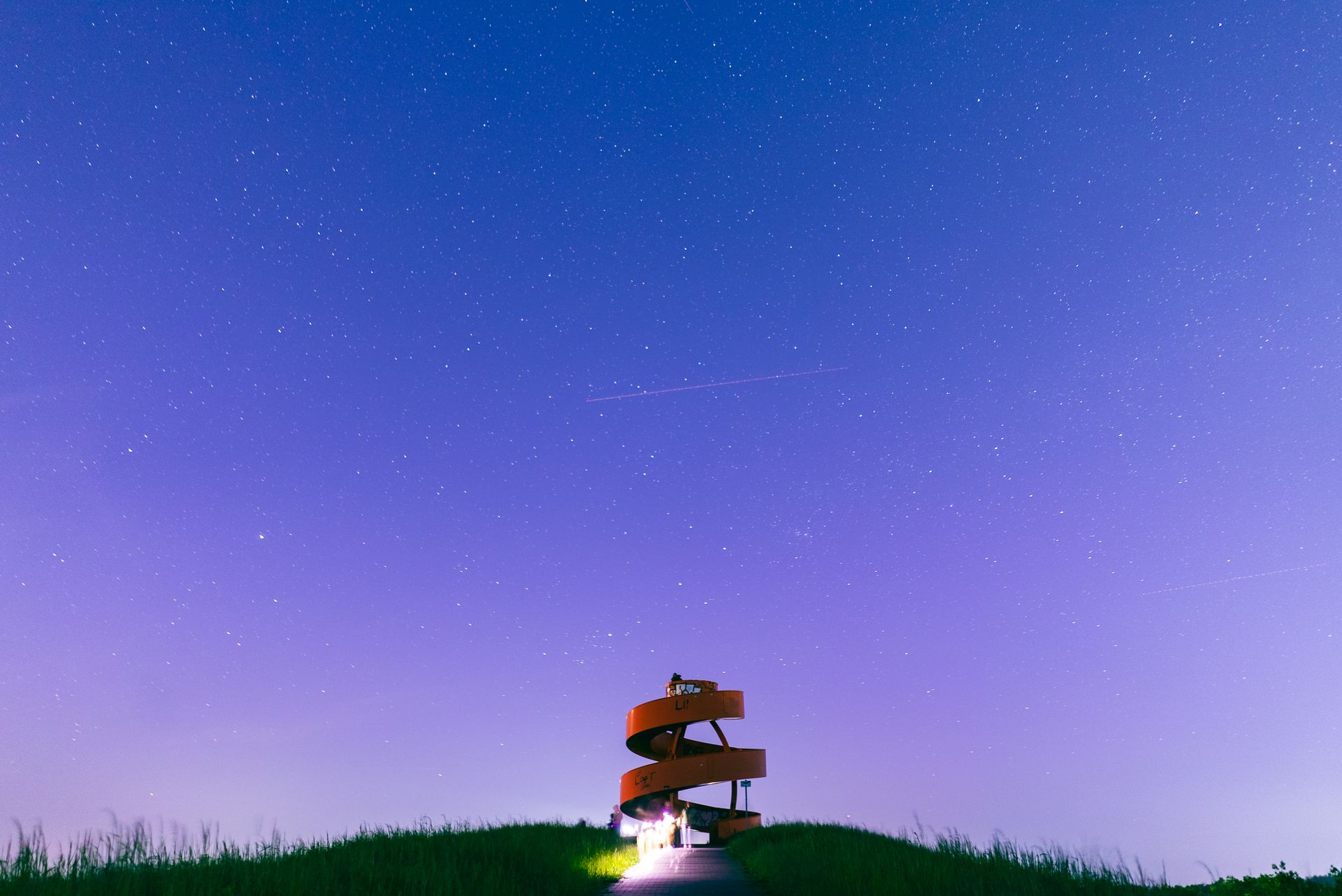 Spiral staircase tower rising from a grassy hill under a star-filled purple sky, representing the four ascending pinnacle cycles of numerology