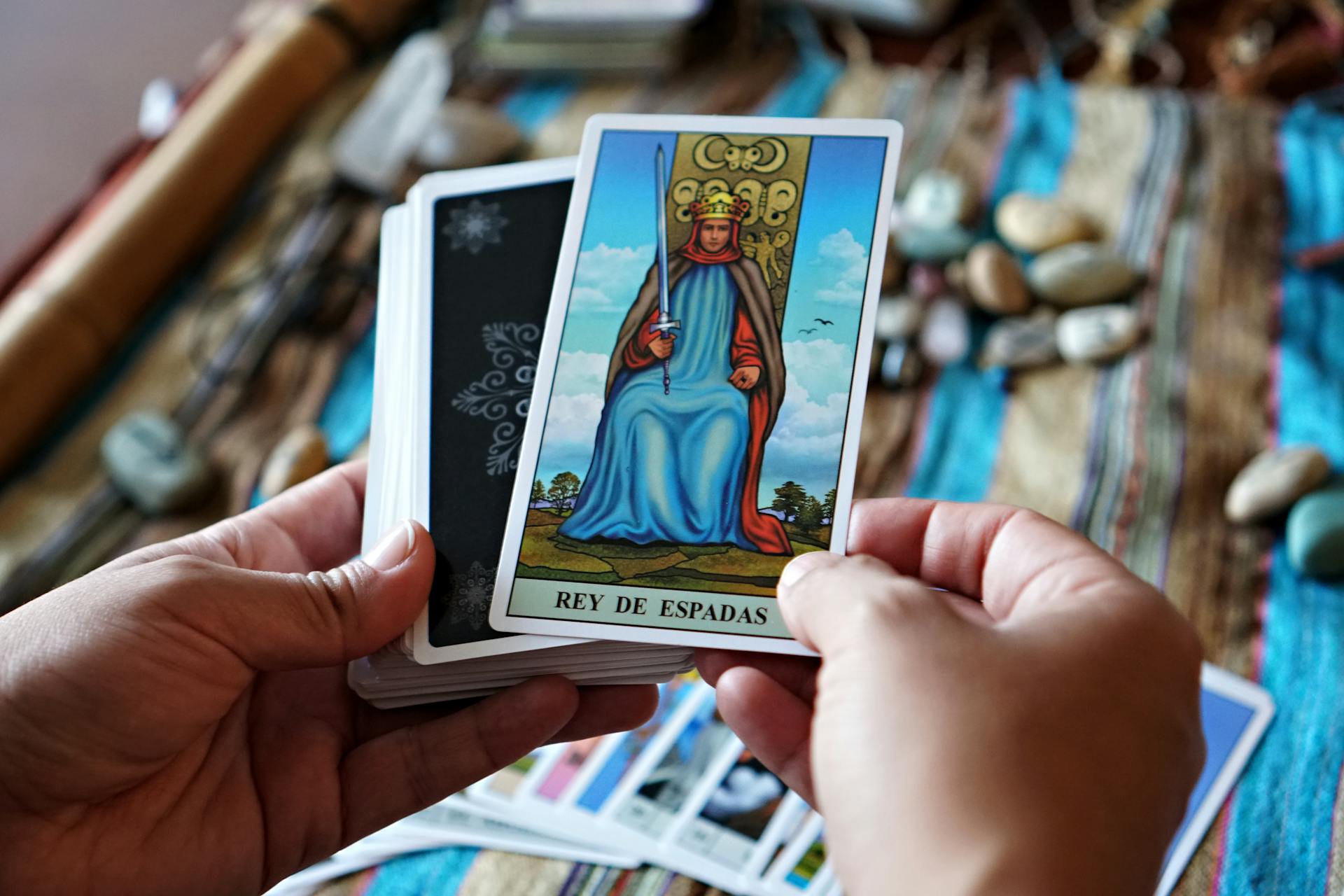 Hands holding a tarot card during a reading session with stones in the background