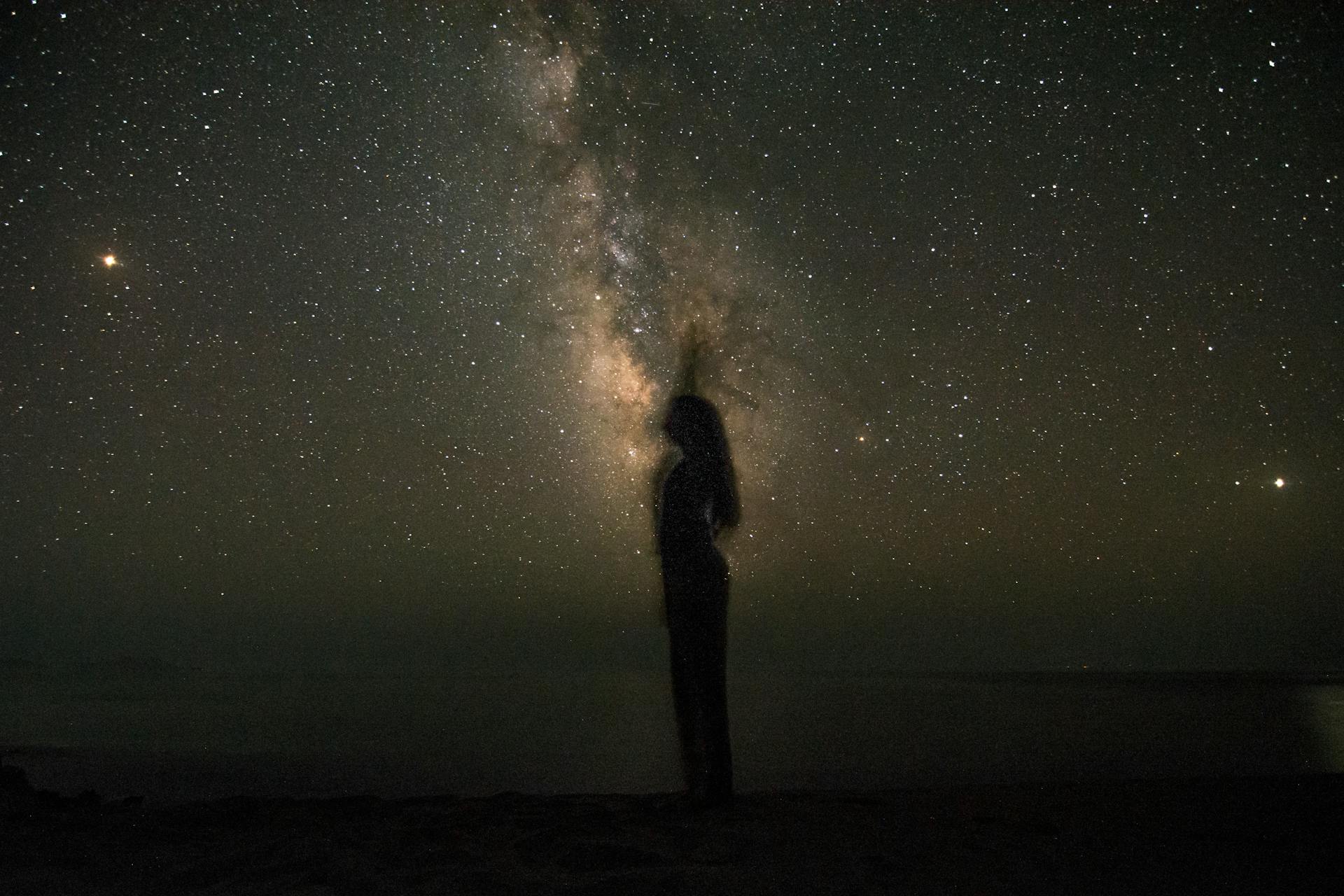 A silhouette standing under the expansive Milky Way representing the cosmic influence of the rising sign on physical appearance