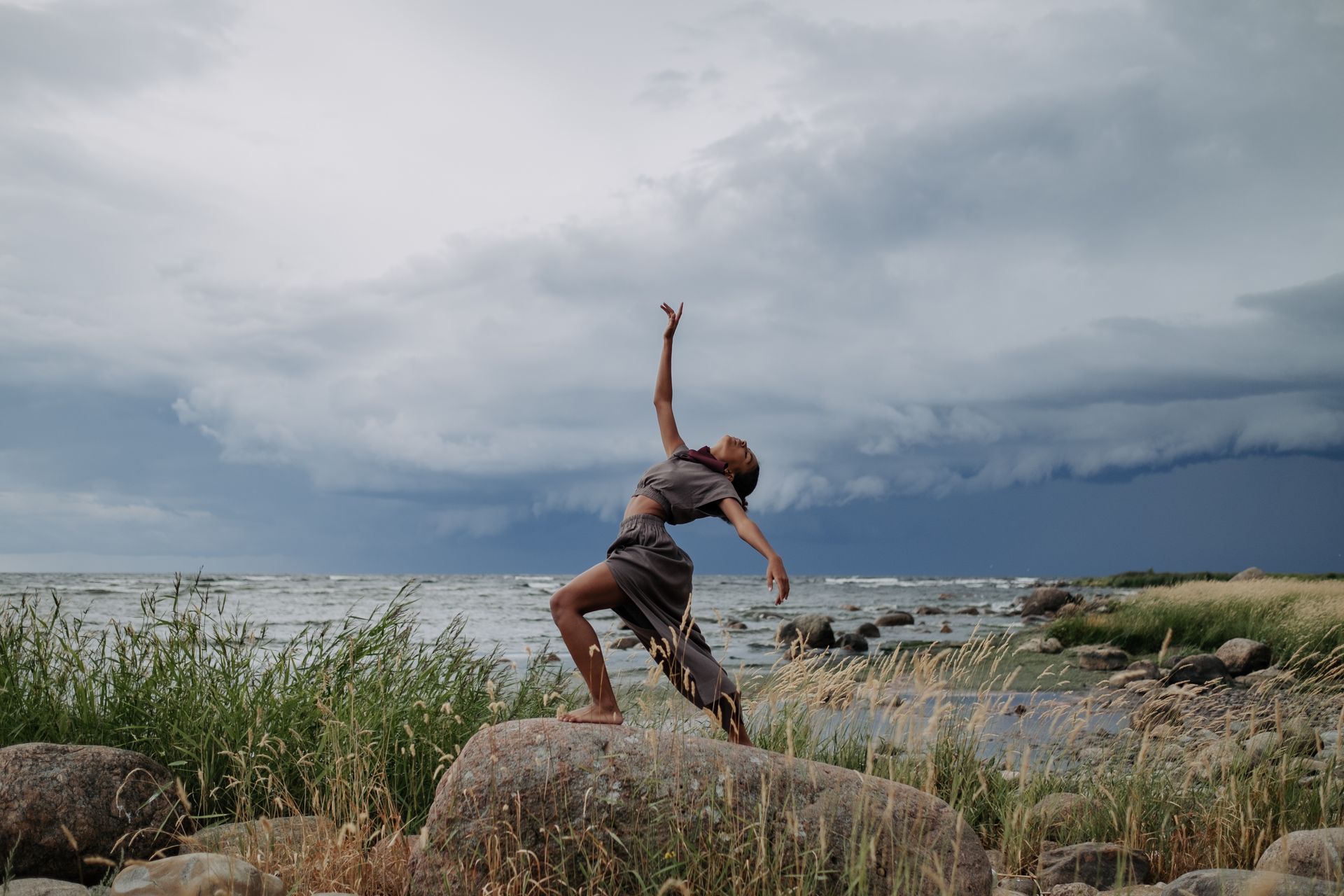 A woman dancing expressively on a rock by the sea, arms flowing, showing the free movement that opens the sacral chakra