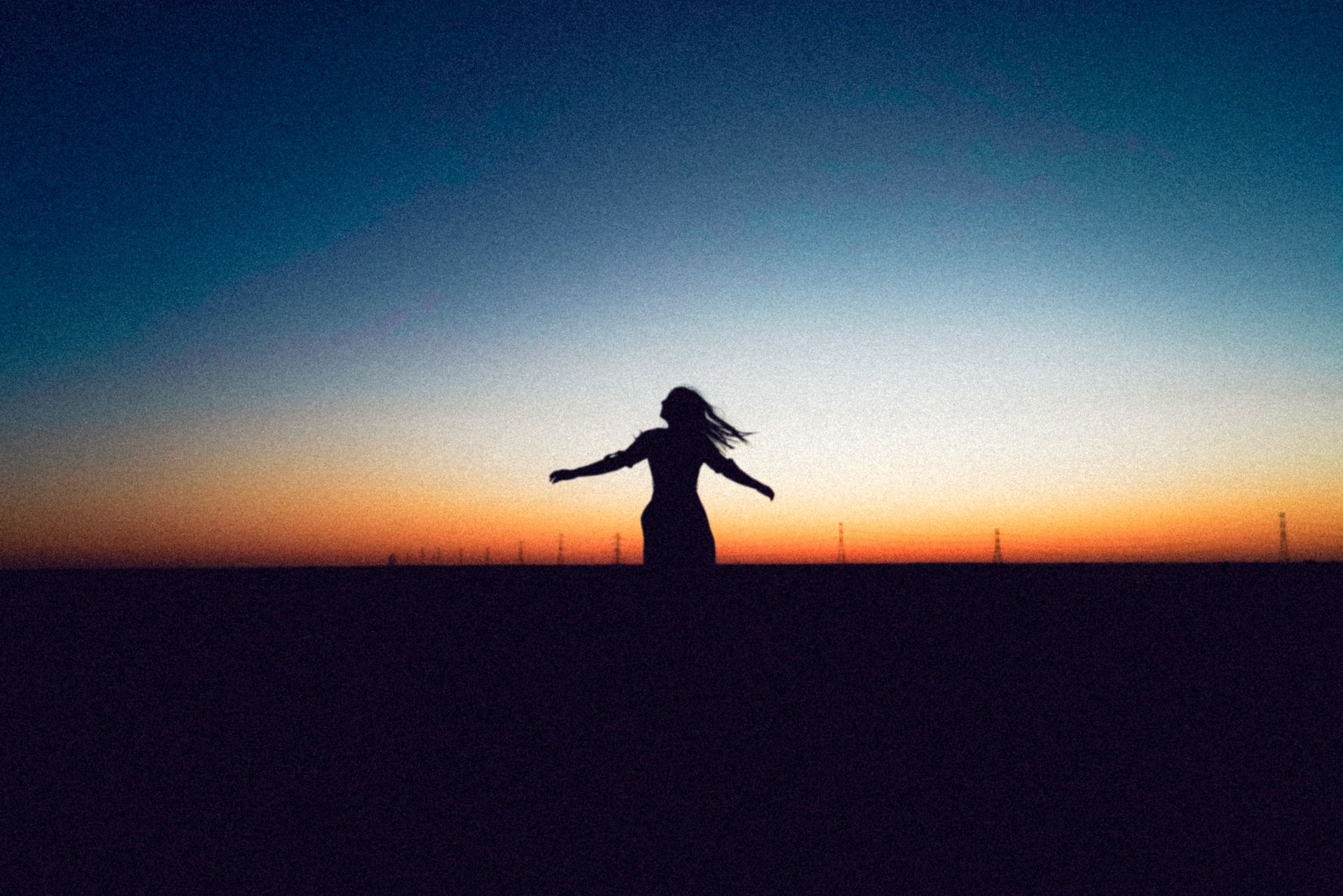 A woman with open arms silhouetted against a glowing orange sunset, moving freely, illustrating the creativity and emotional flow of a balanced sacral chakra