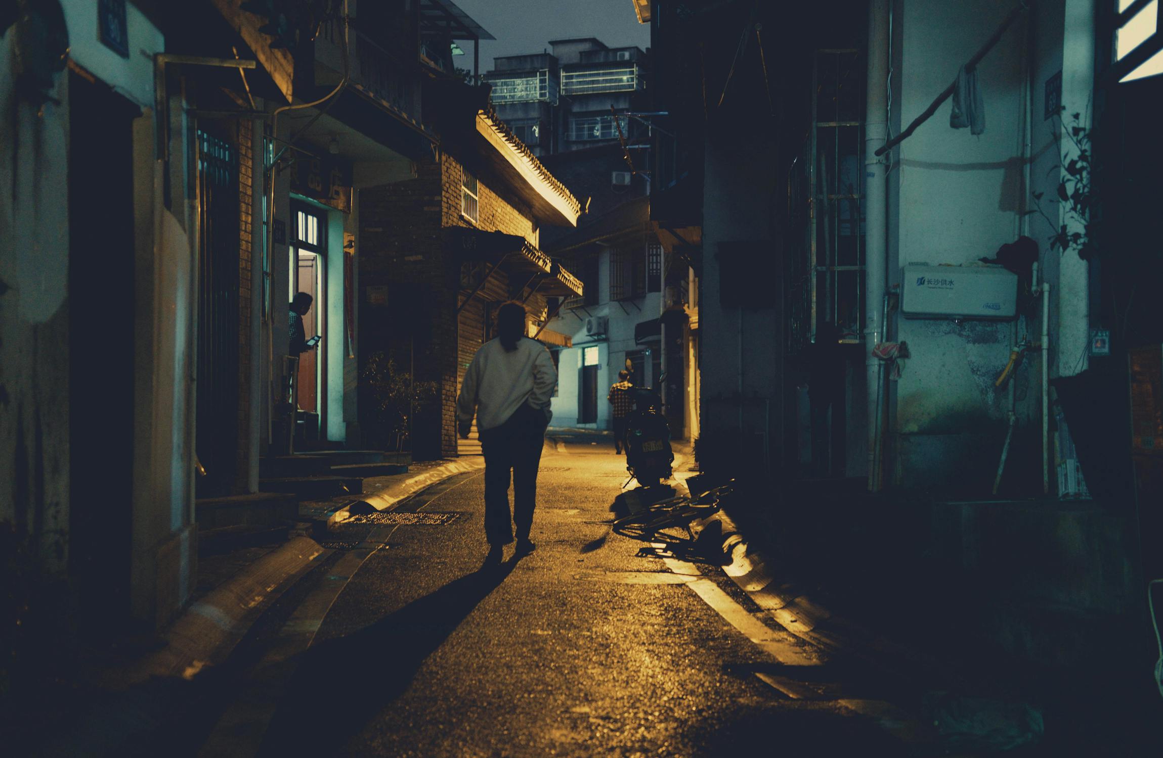 A mysterious figure walking through a dimly lit urban alley at night creating a dramatic shadow that evokes the stealth and secrecy of the Seven of Swords