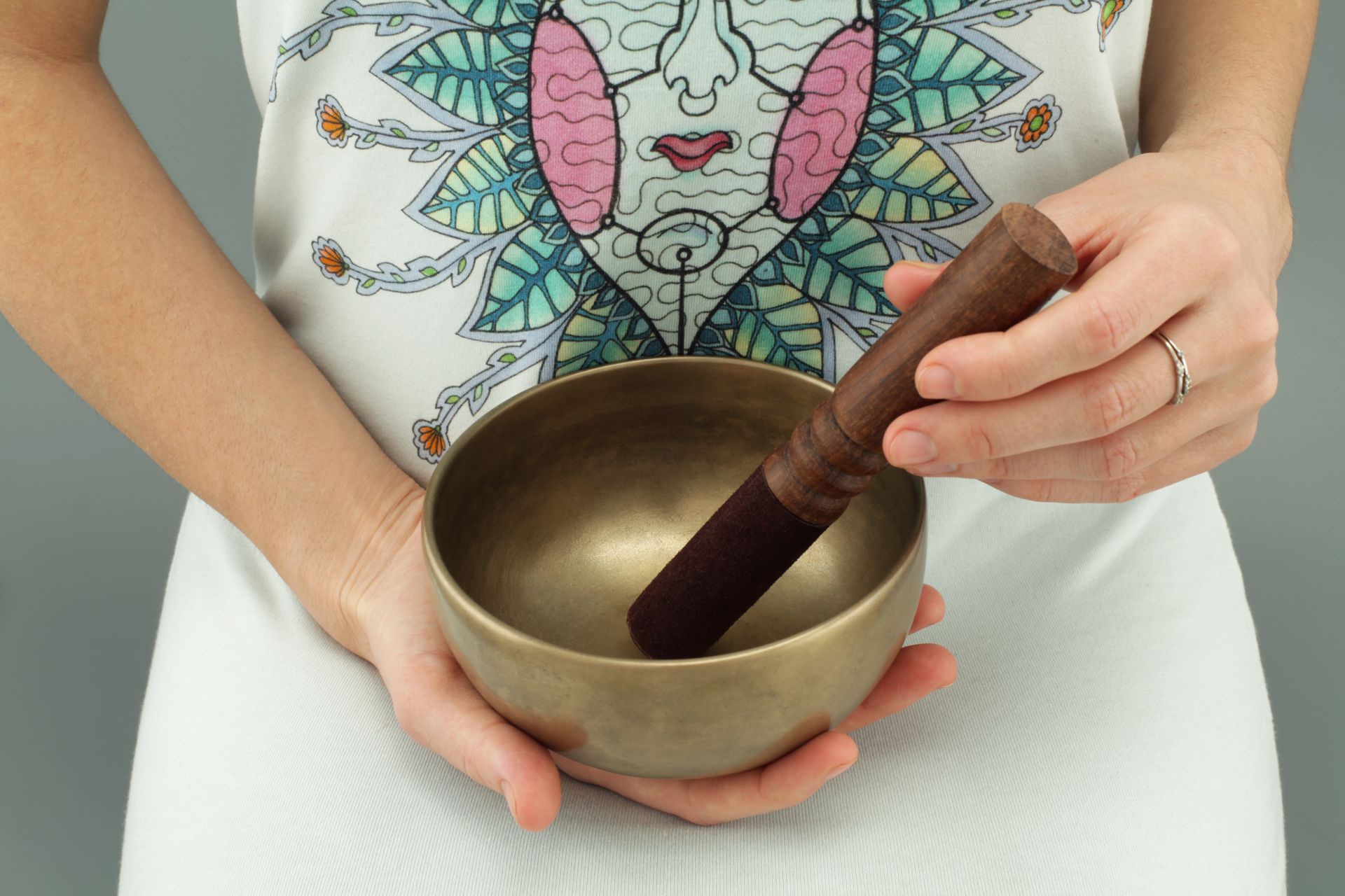 A metal singing bowl with its mallet resting on a soft neutral cloth