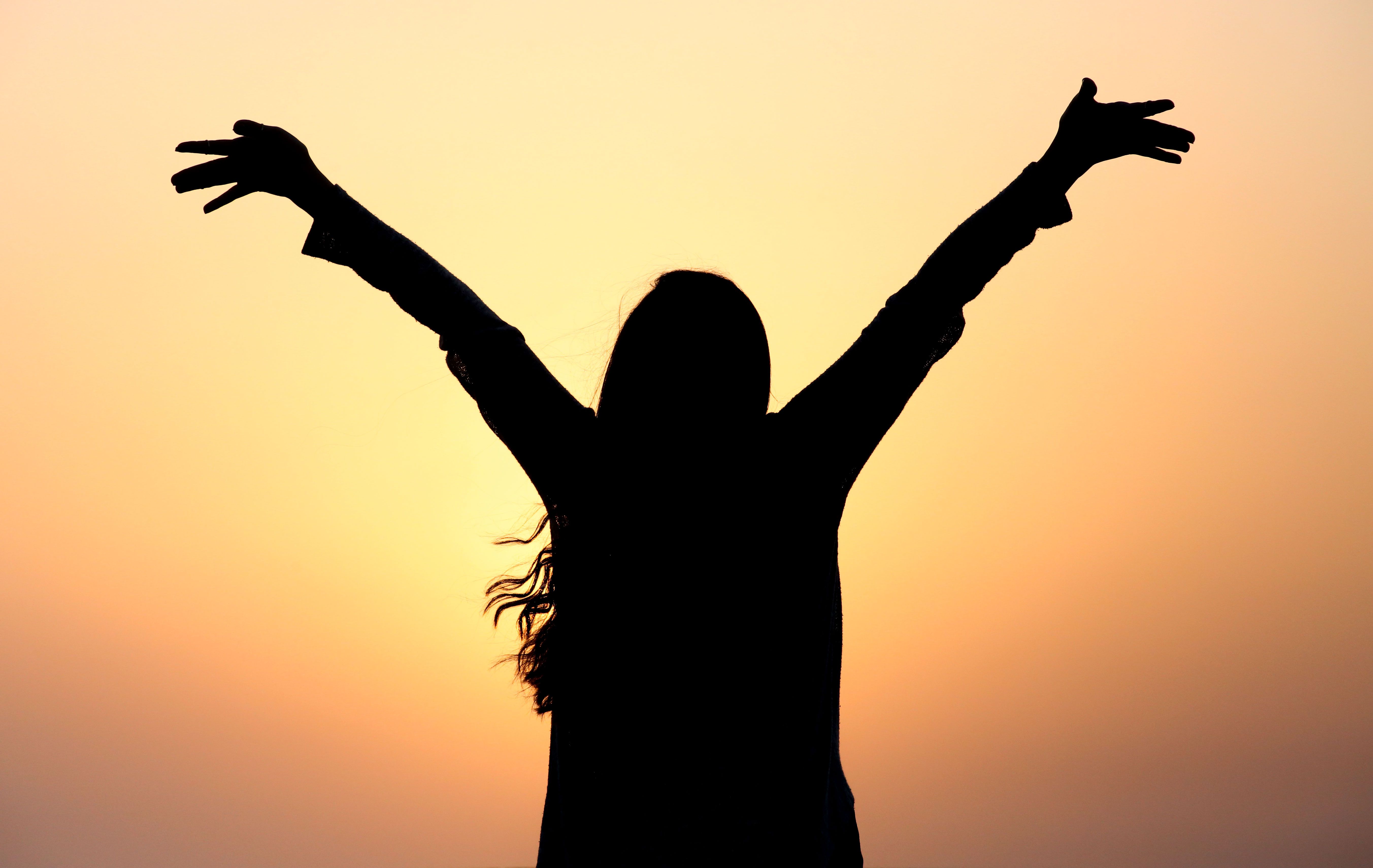 A confident person standing with arms raised toward a bright sunrise, radiating the personal power and self-assurance of a balanced solar plexus chakra