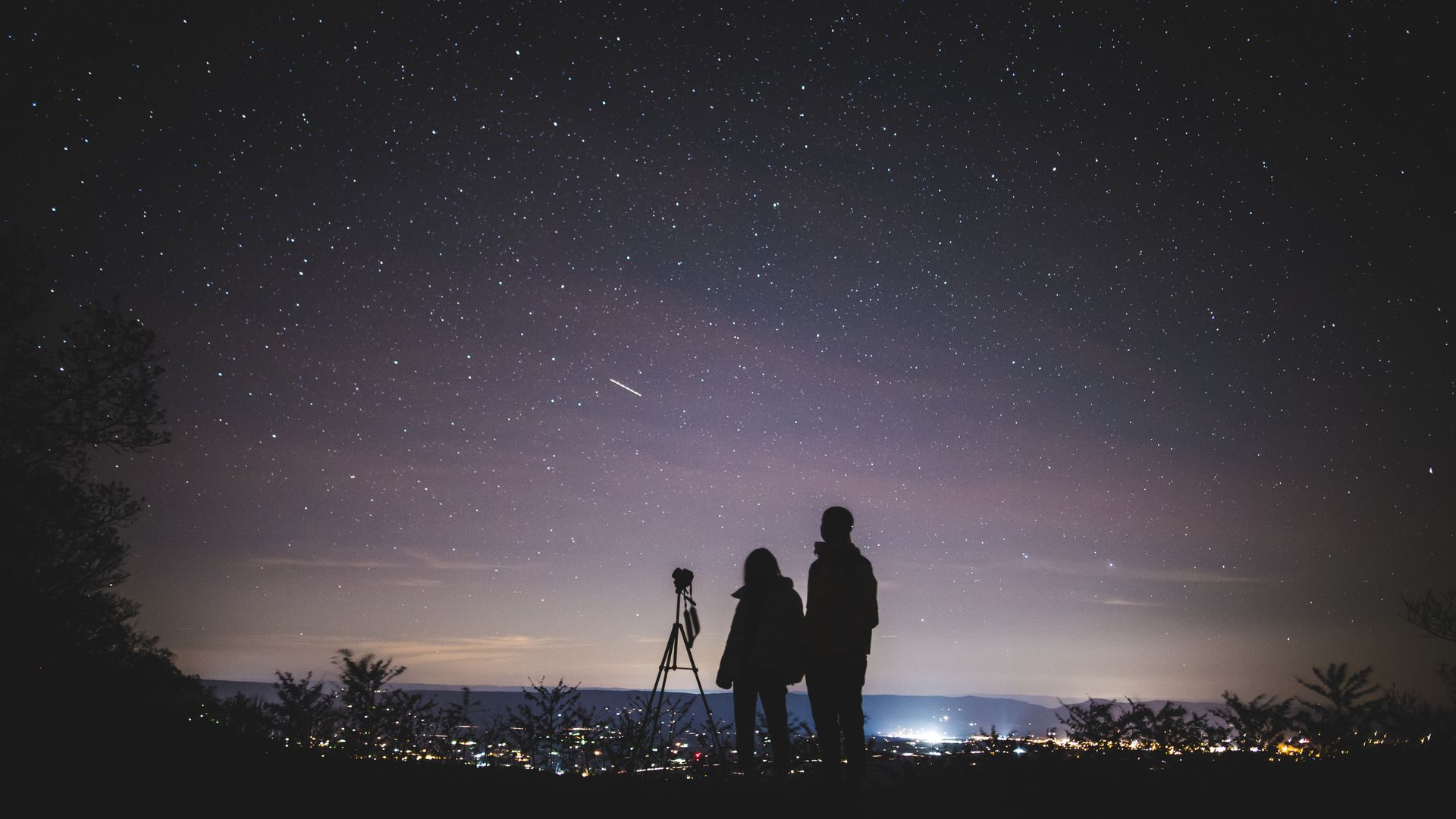 Silhouette of a couple standing close together under a star-filled night sky, representing two birth charts forming synastry aspects