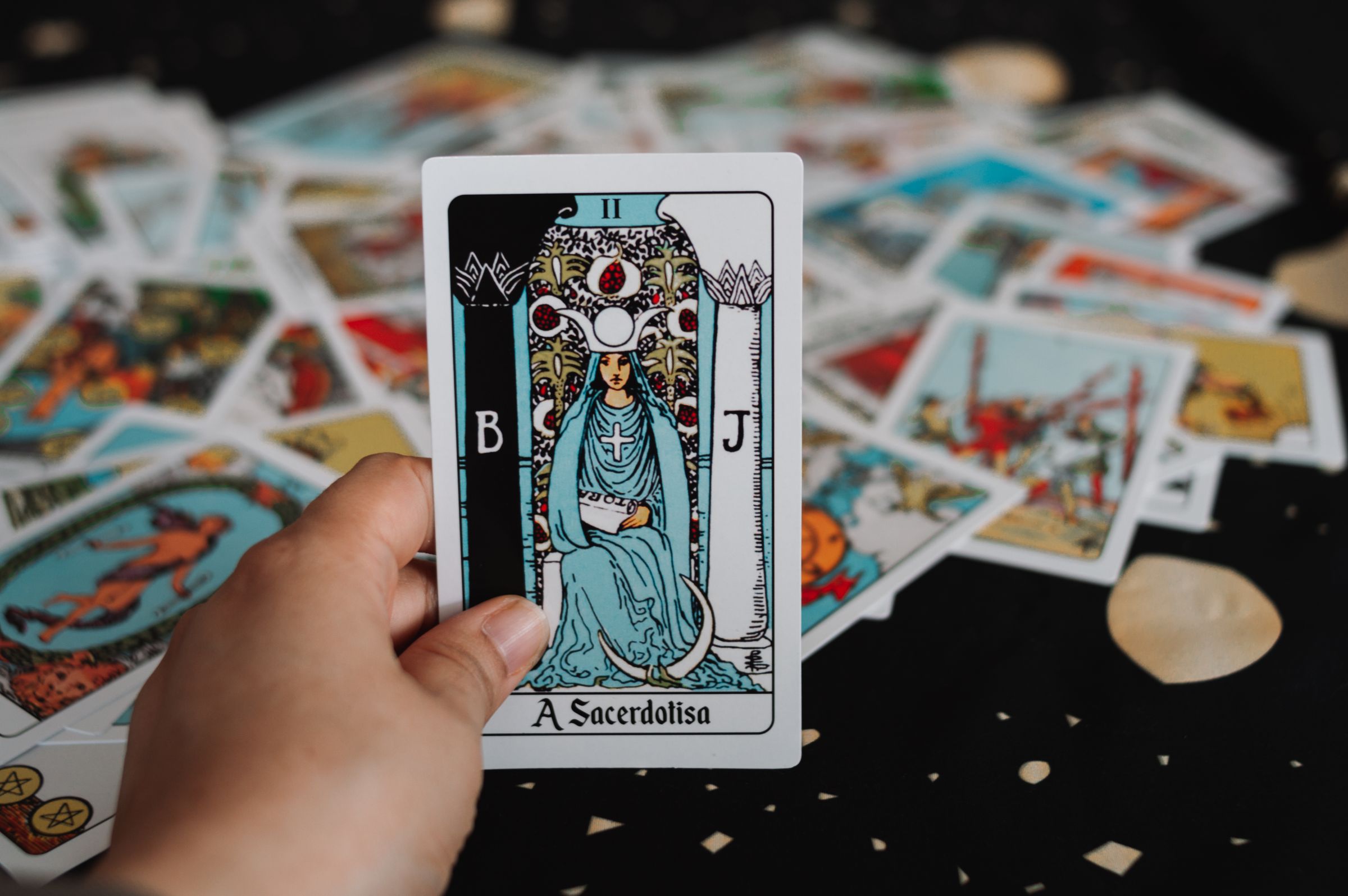 A hand holding the High Priestess card above a scattered tarot deck