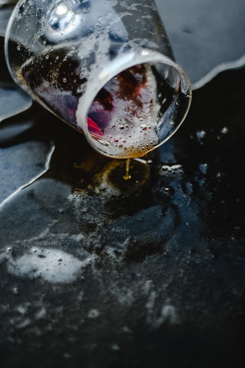 Close-up of a spilled glass creating reflections on a dark surface capturing the sense of loss and what has been poured out that defines the Five of Cups