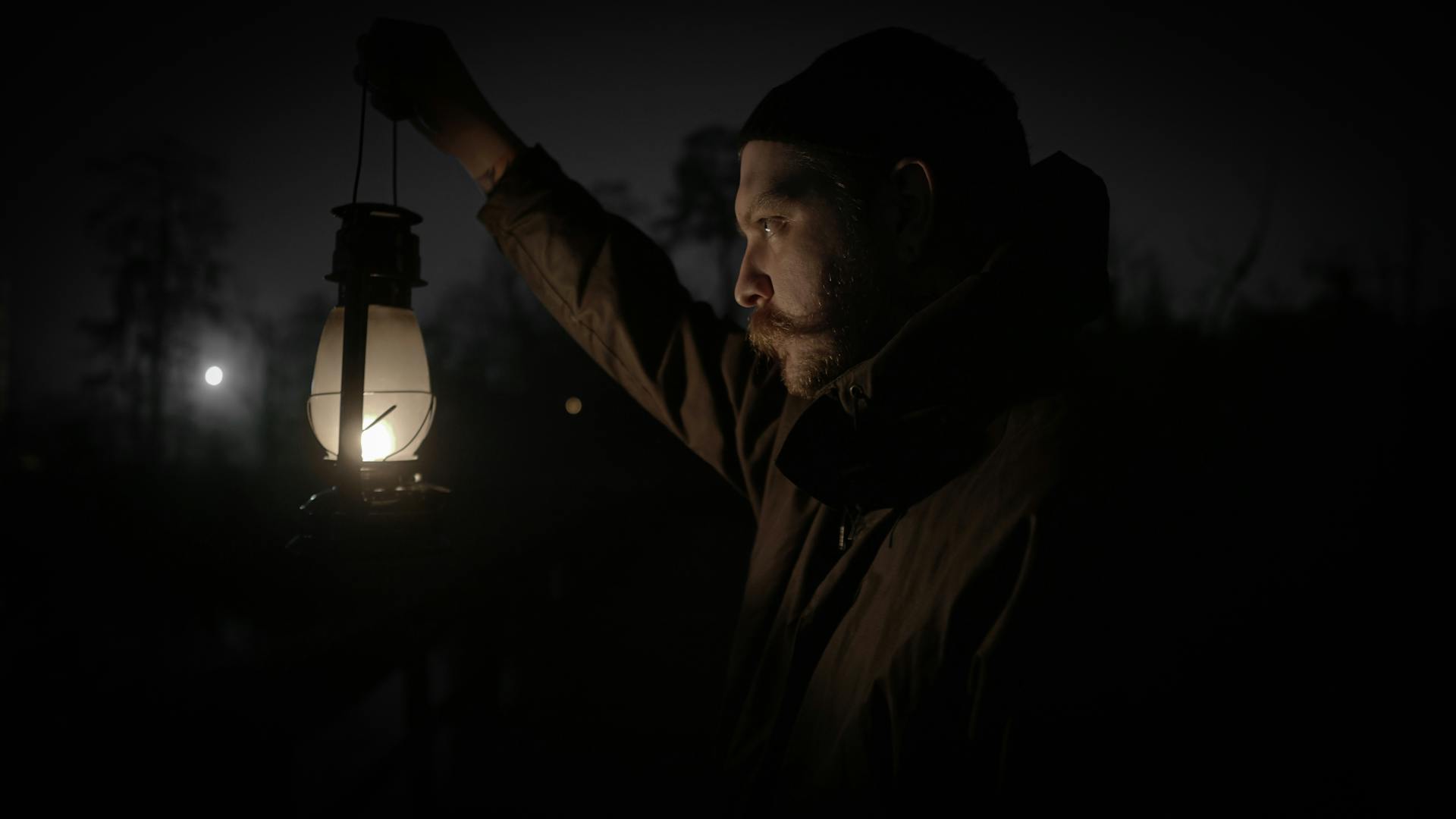 A man with a lantern explores the outdoors during a dark night representing The Hermit's solitary quest for truth