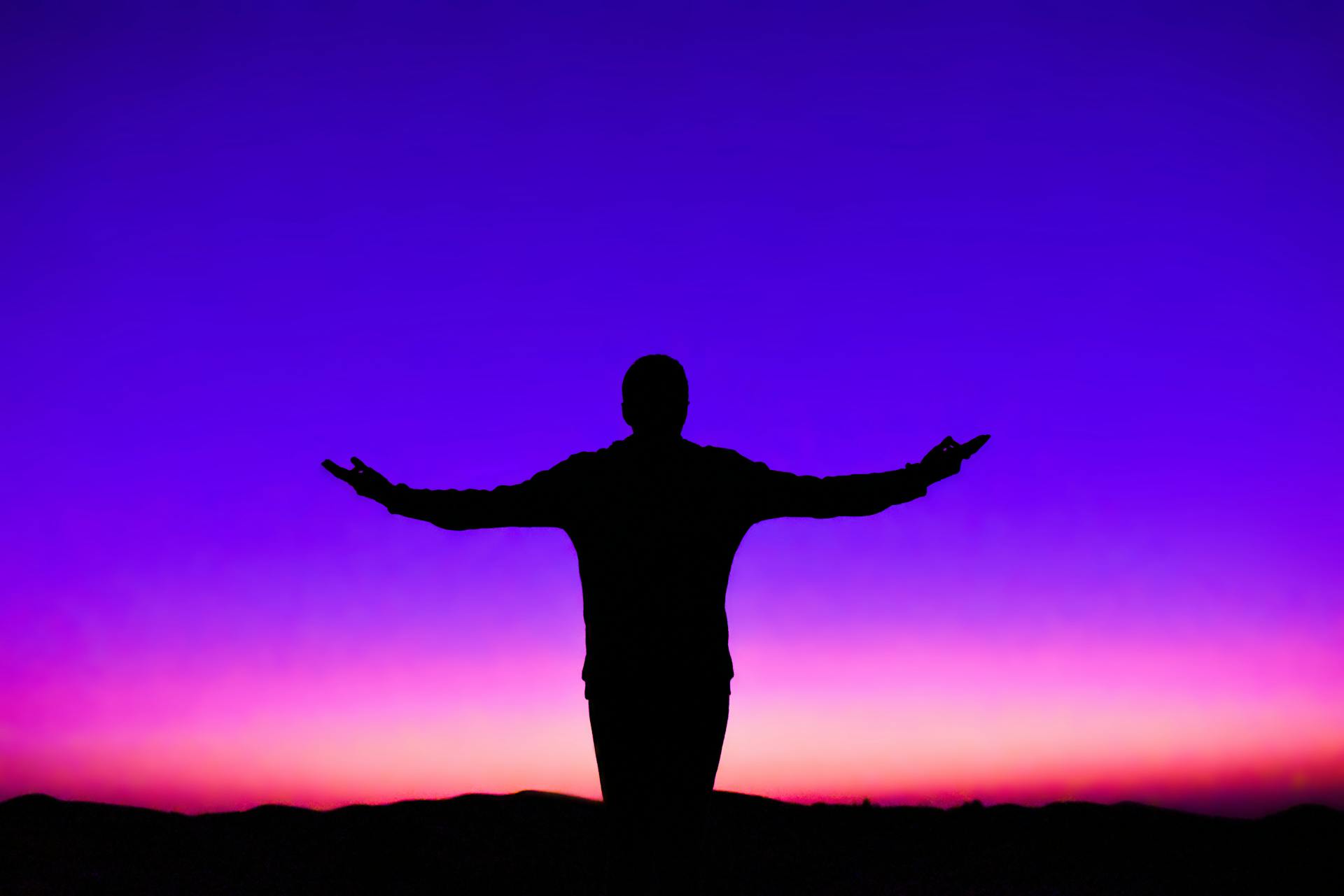 Silhouette of a person with outstretched arms against a vivid sunset sky representing the moment of spiritual awakening