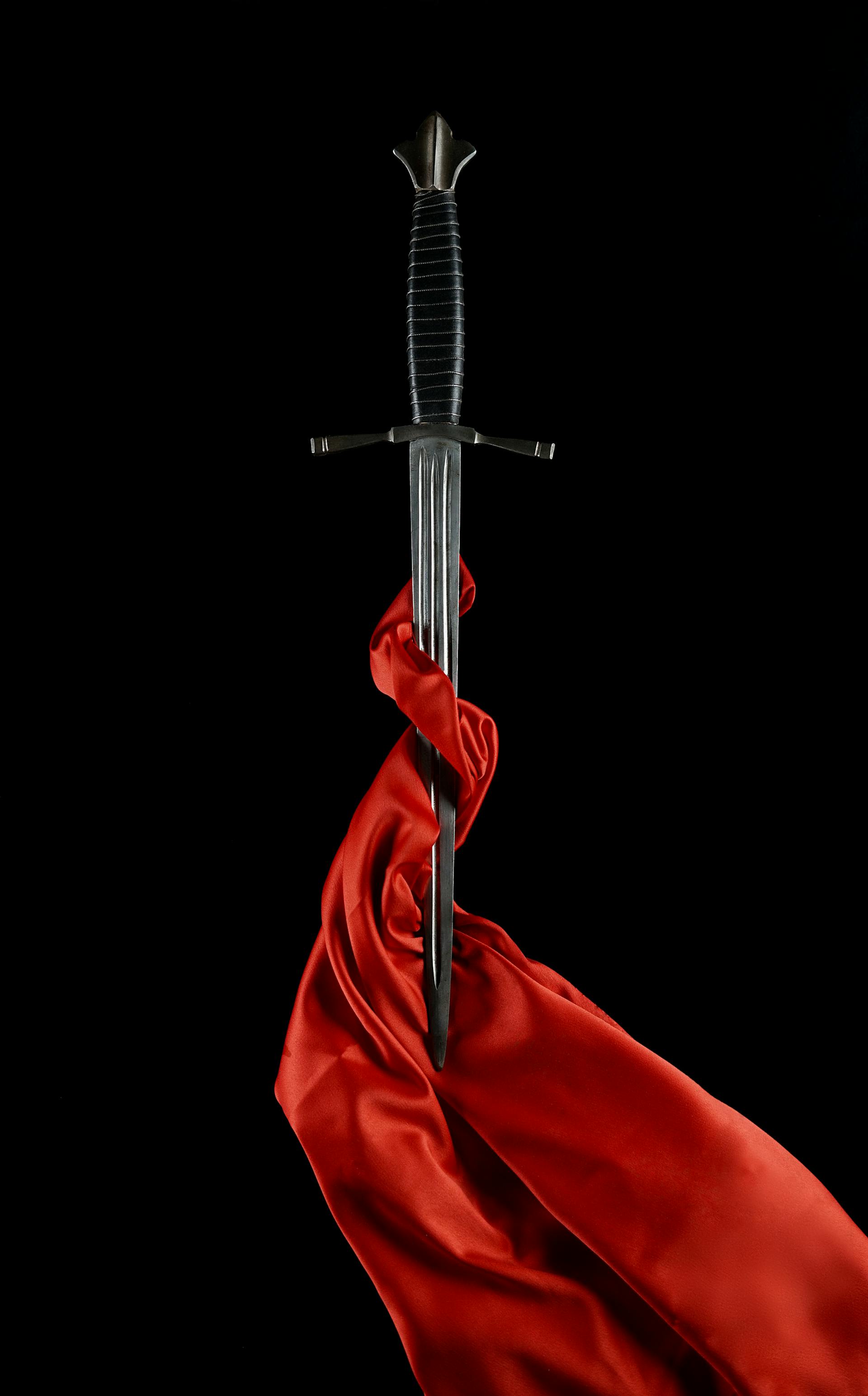 A medieval sword wrapped in red silk against a dark background representing the sharp clarity of Justice