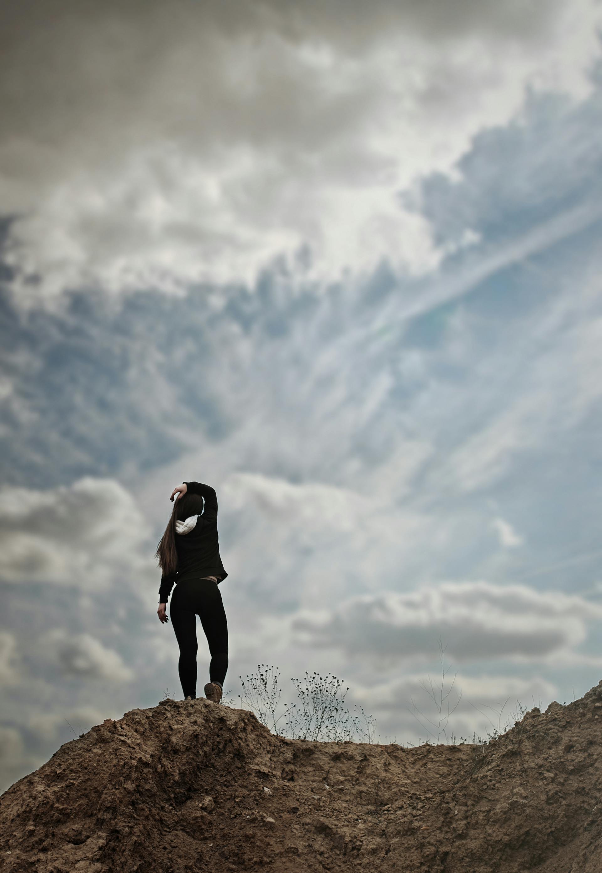 A woman stands on a rocky hill gazing at a dramatic sky symbolizing the courage to hold firm when challenged by the Seven of Wands