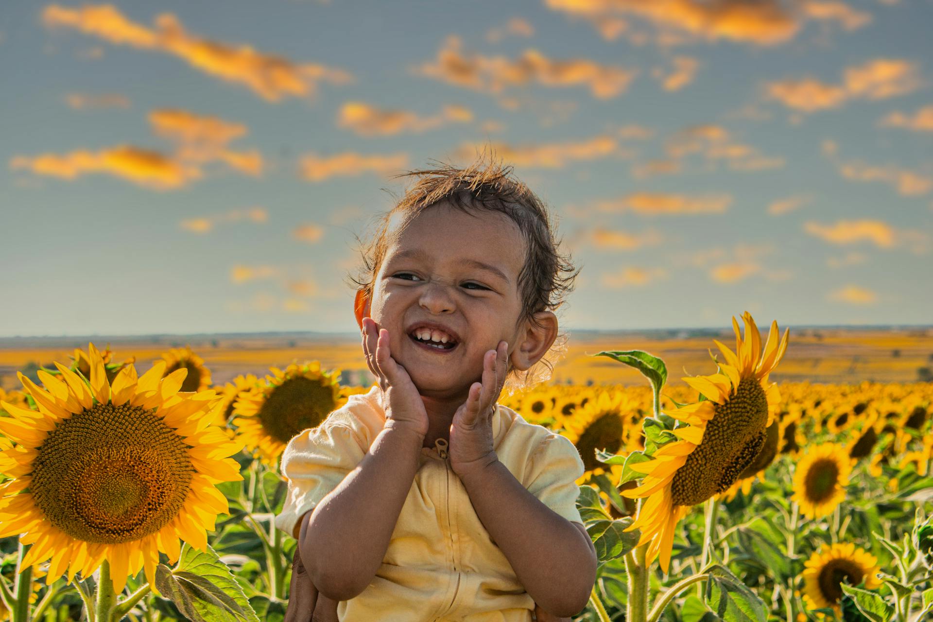 A smiling child in a vibrant sunflower field during sunset radiating happiness and warmth