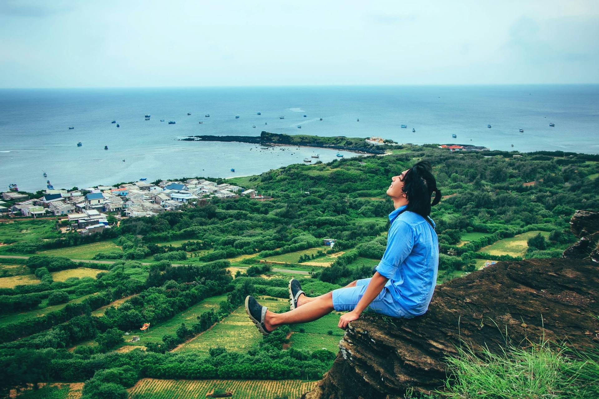 A young man sits peacefully on a cliff enjoying the scenic ocean view embodying the forward-looking confidence of the Three of Wands